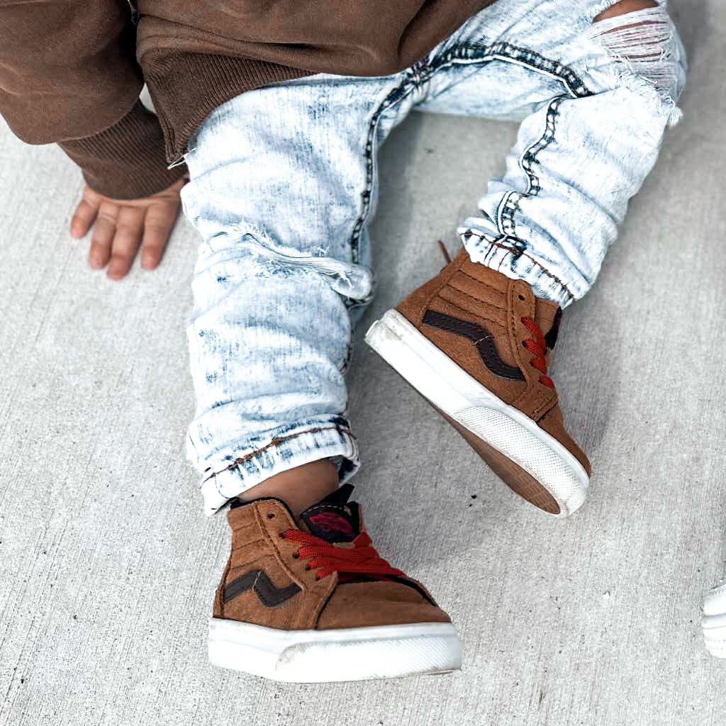 Child wearing brown shoes and light blue distressed jeans on a gray surface