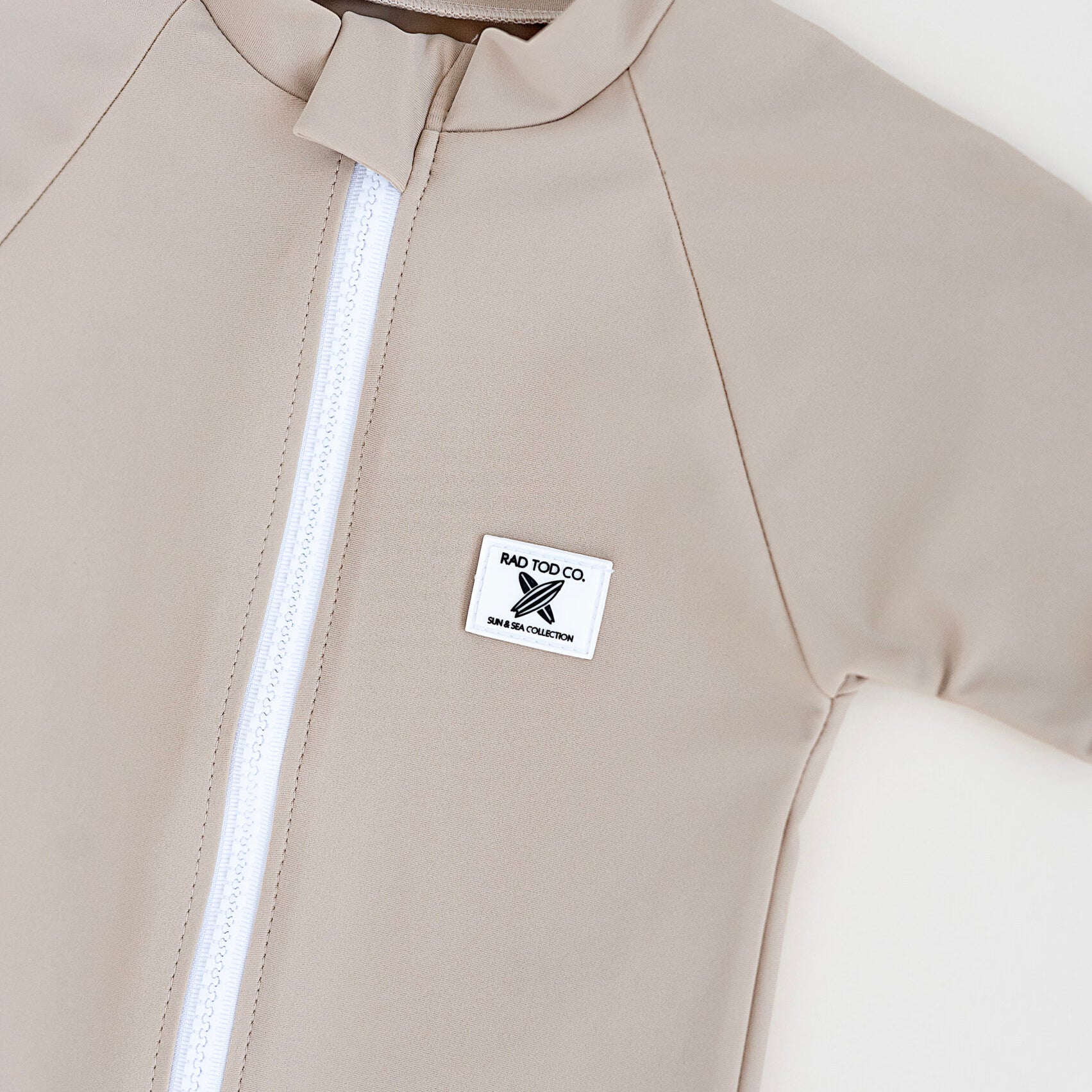details on Rad Toddlers 'Sand' Rashguard Shirt with front zipper and UPF 50+ protection, perfect for pairing with board shorts for water activities.