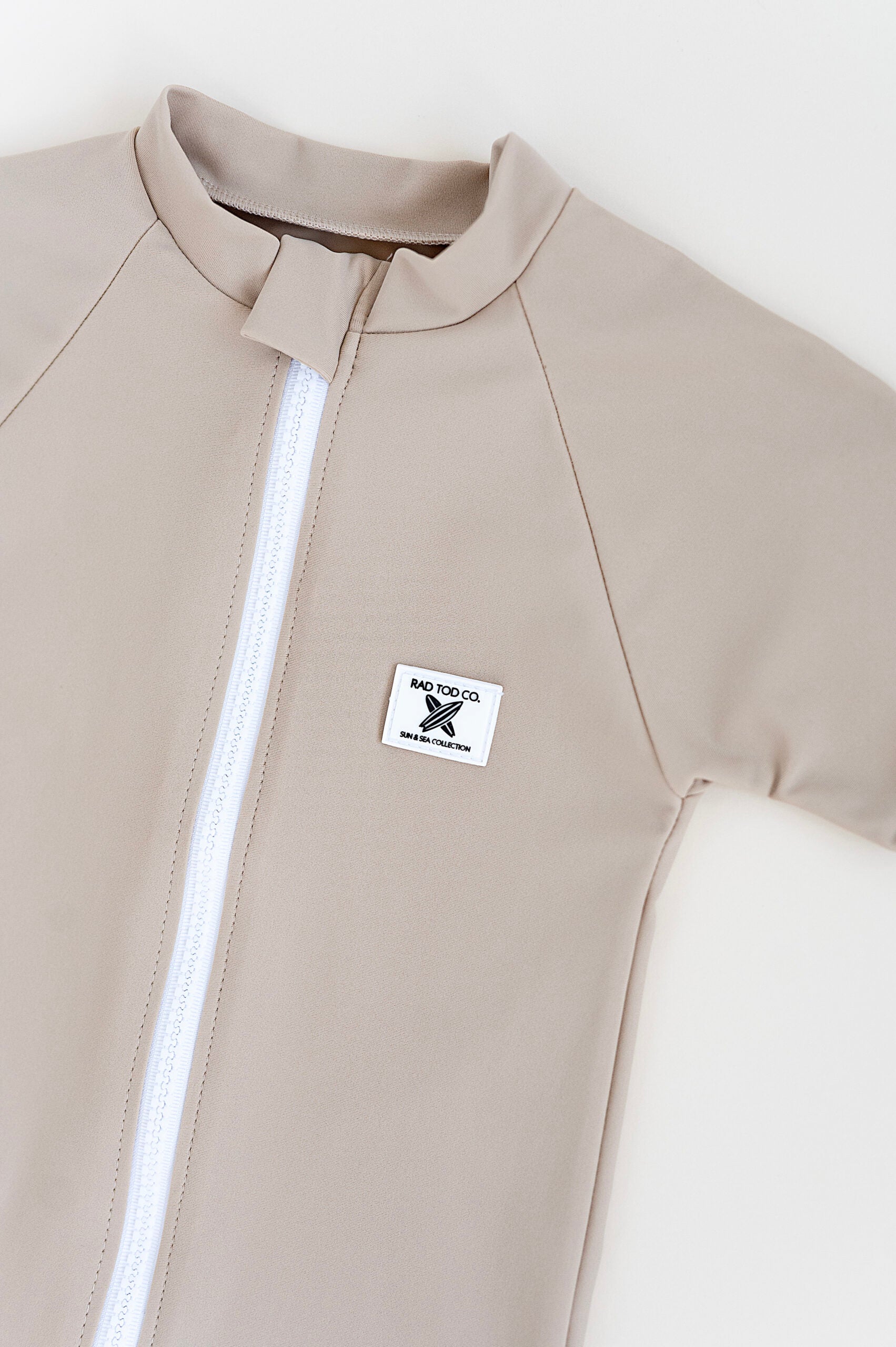details on Rad Toddlers 'Sand' Rashguard Shirt with front zipper and UPF 50+ protection, perfect for pairing with board shorts for water activities.