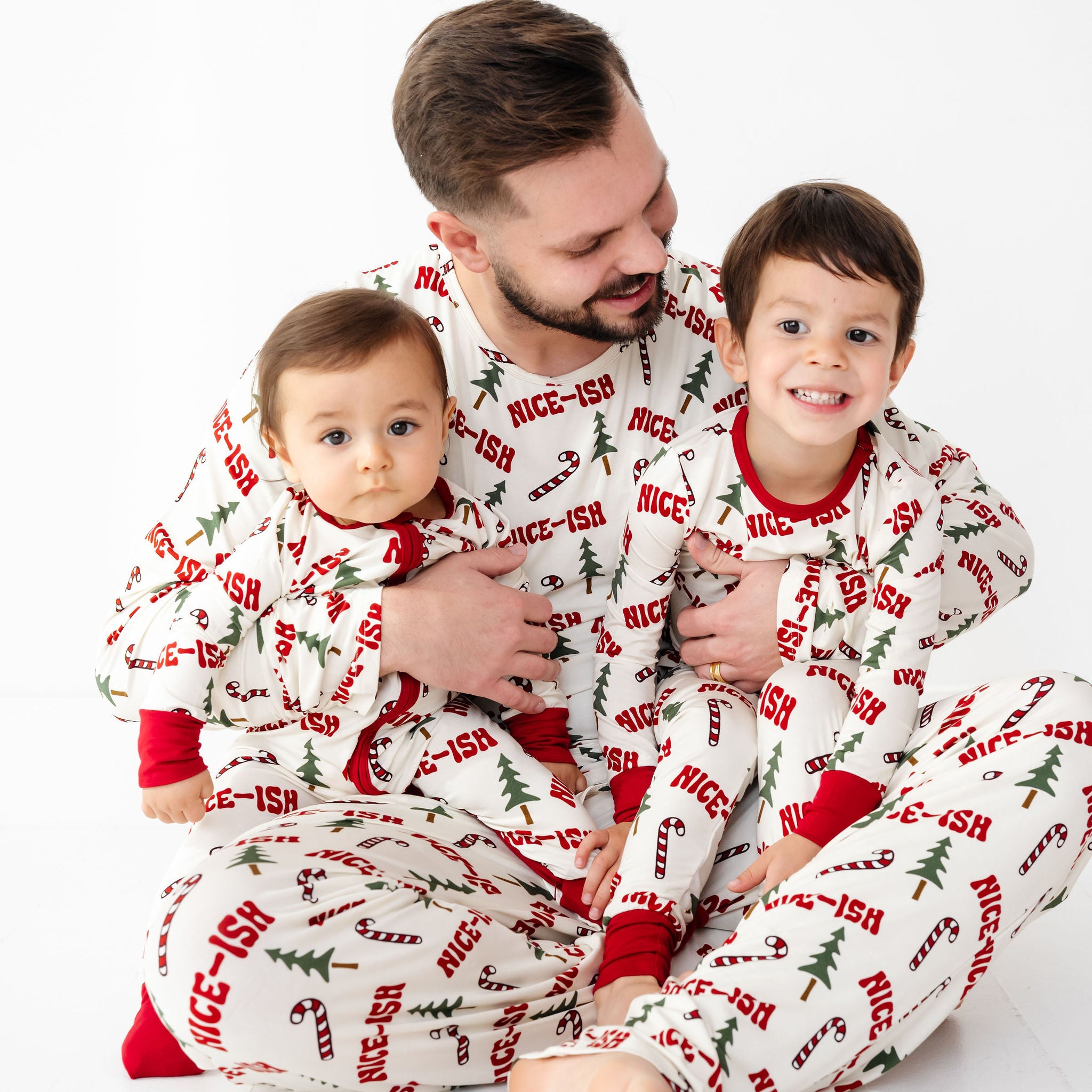 Man and two children wearing matching Christmas-themed pajamas on a white background