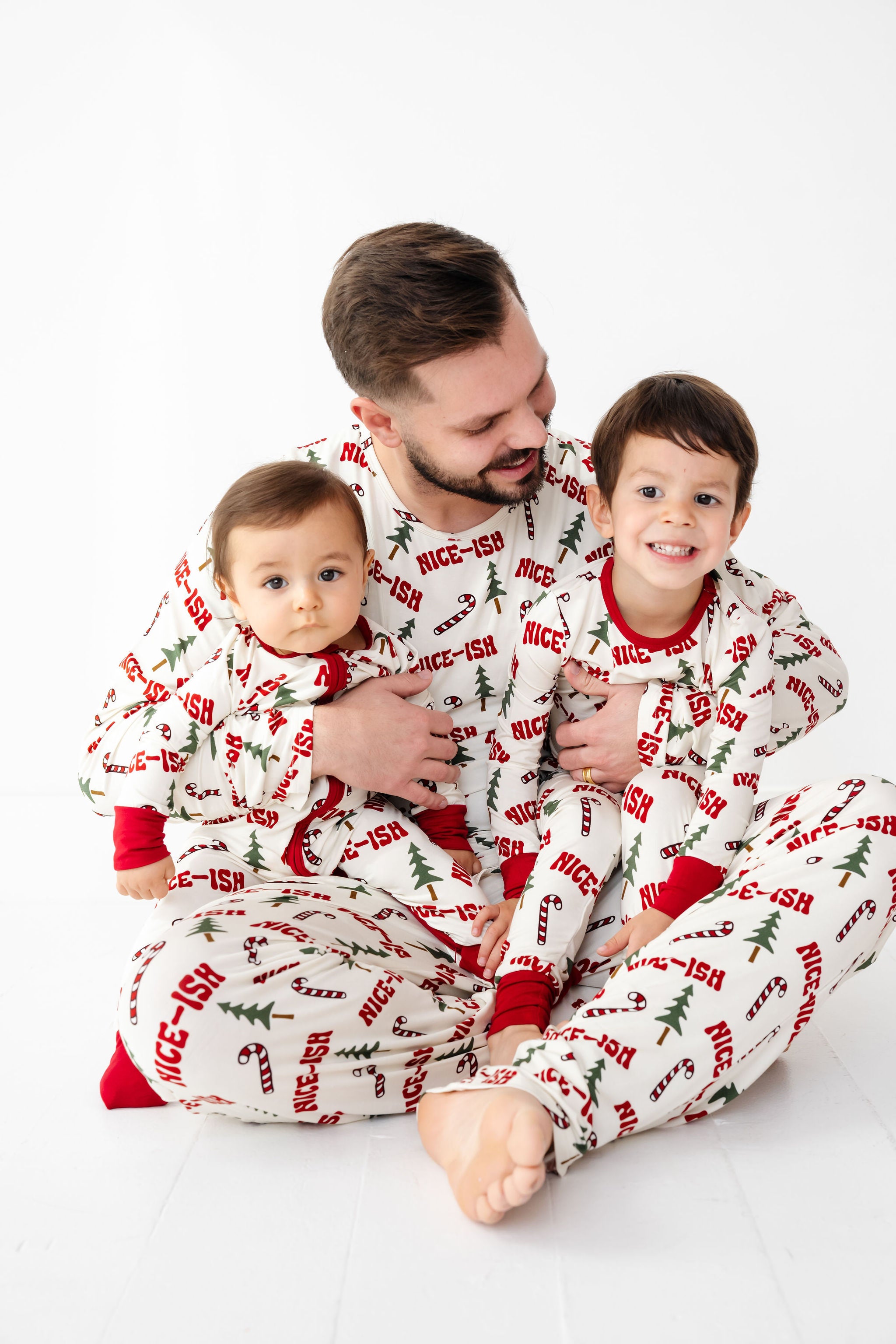 Man and two children wearing matching Christmas-themed pajamas on a white background