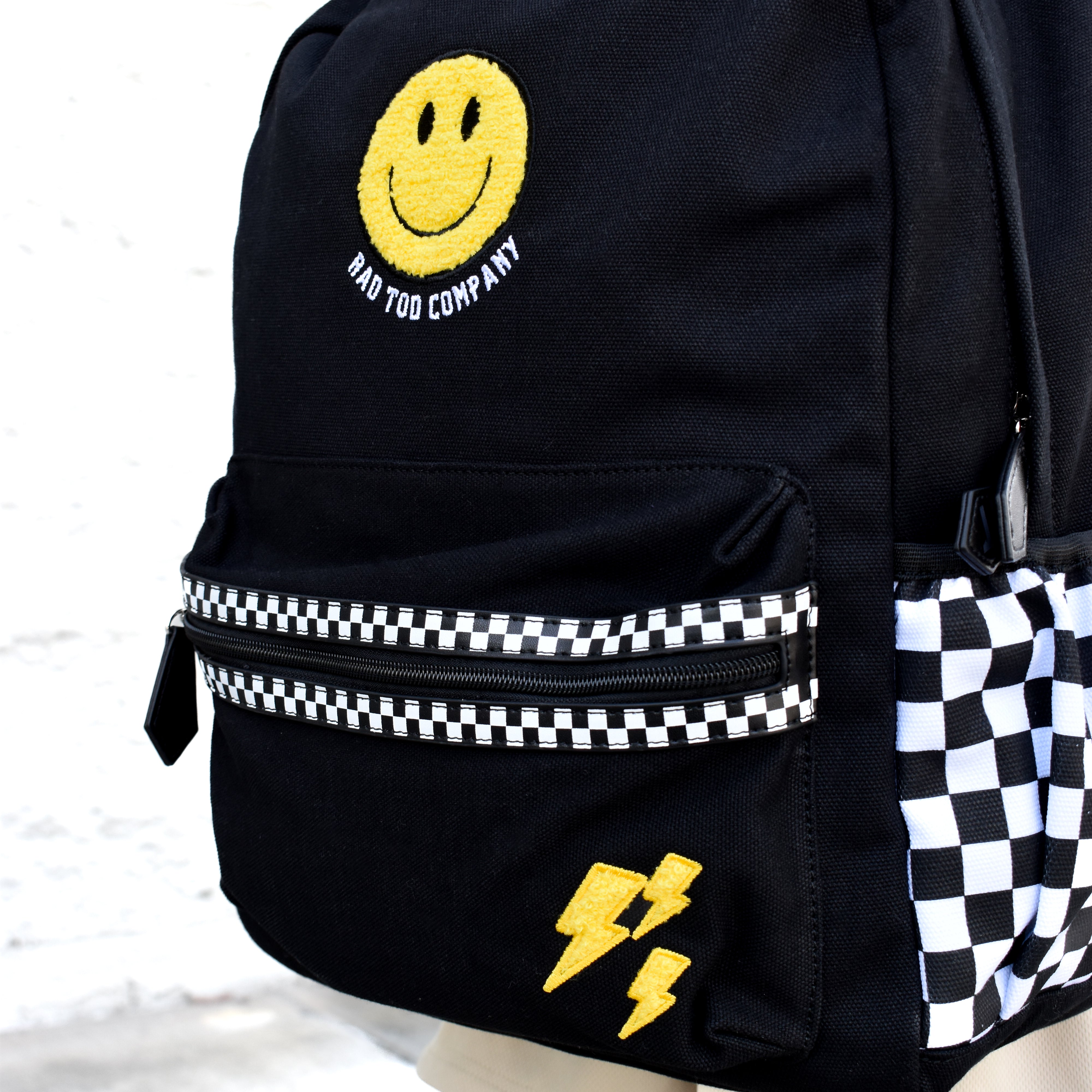 Black backpack with smiley face and lightning bolt design on a checkered background