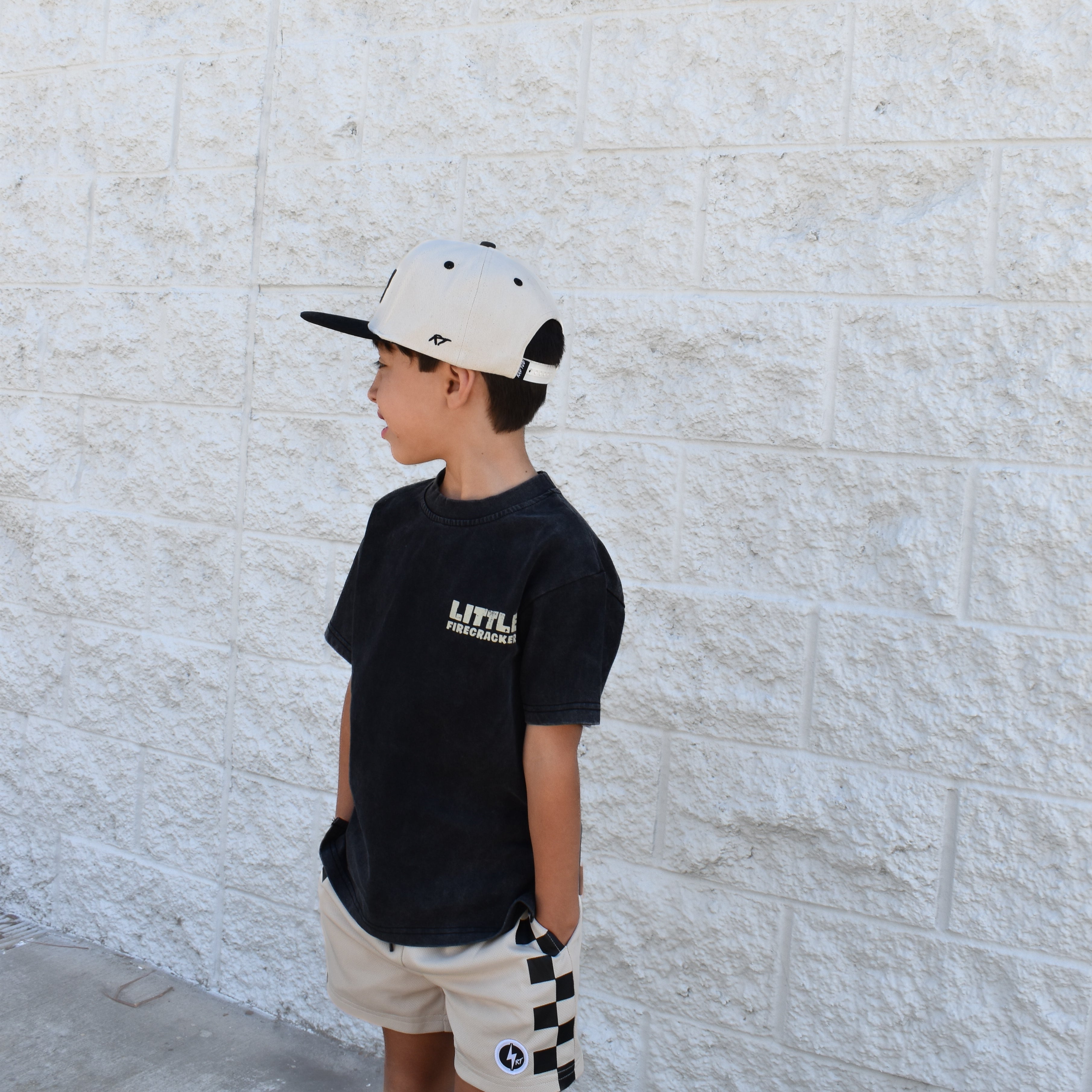 Kid wearing the Little Firecracker graphic tee on a black acid wash shirt with patriotic red, white, and blue design.