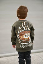 Child wearing a green sweatshirt with a graphic design and brown beanie, standing against a plain background.