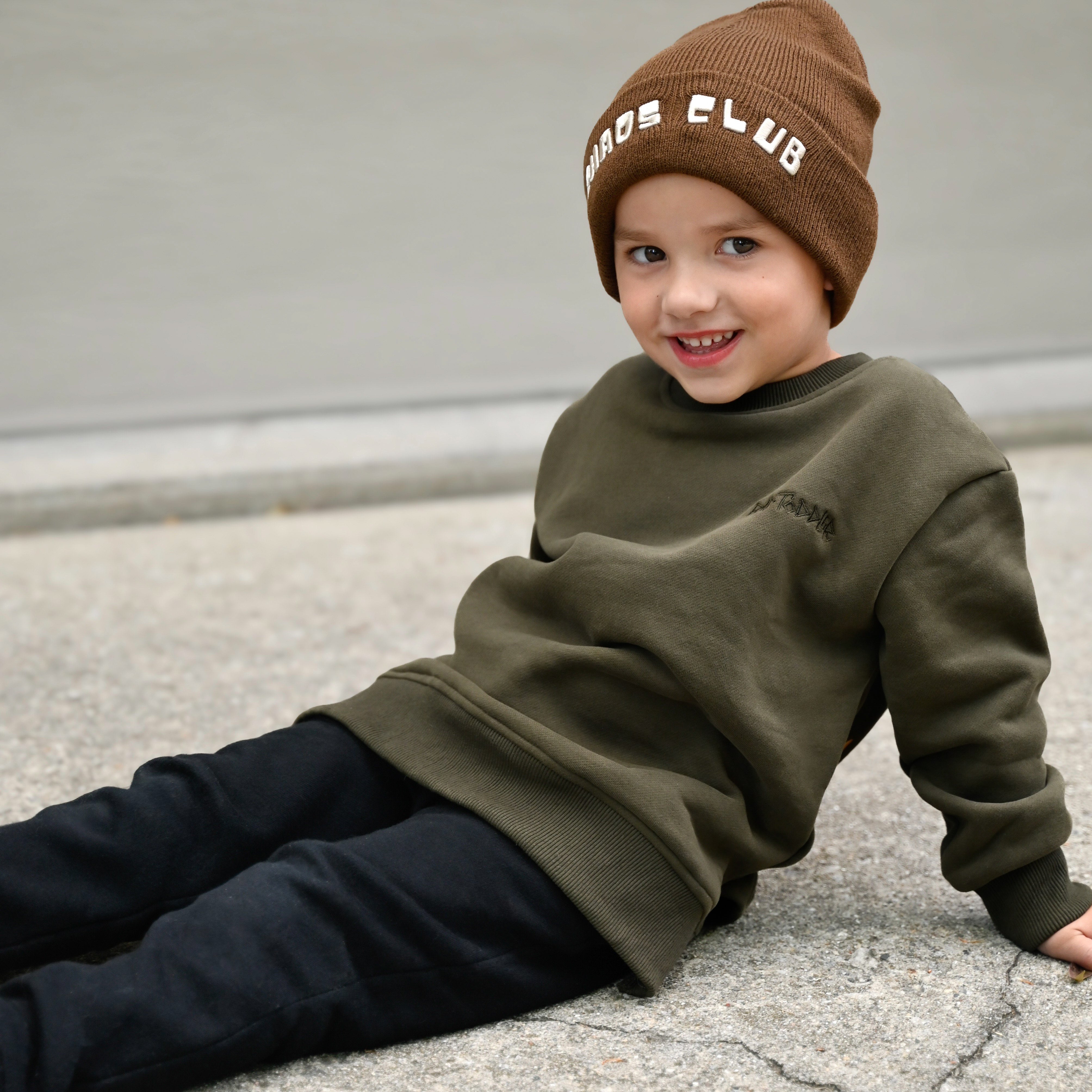 Child wearing dark green Flaming Fast crewneck with helmet and flaming skull graphic