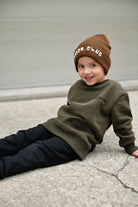 Child wearing dark green Flaming Fast crewneck with helmet and flaming skull graphic