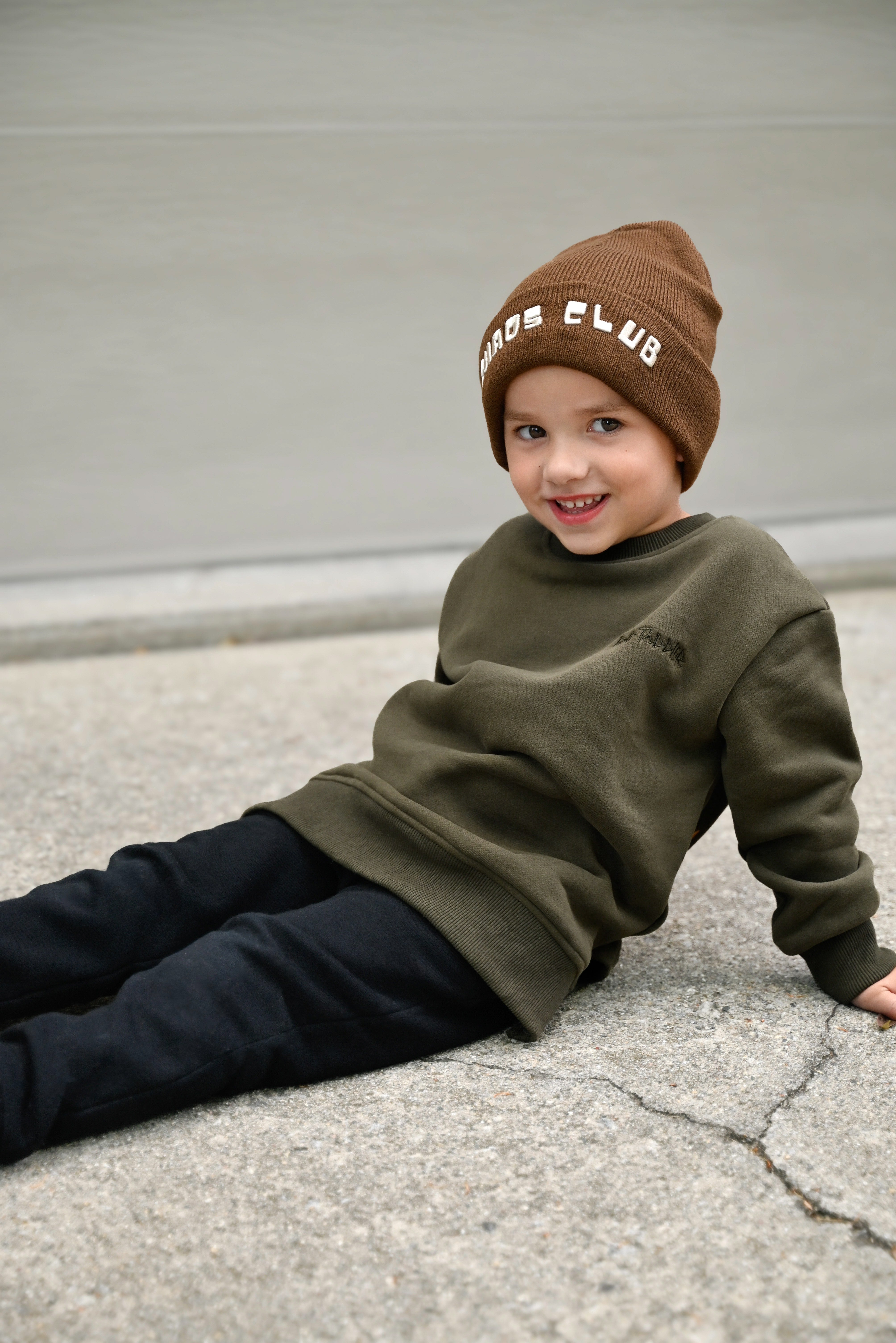 Child wearing dark green Flaming Fast crewneck with helmet and flaming skull graphic