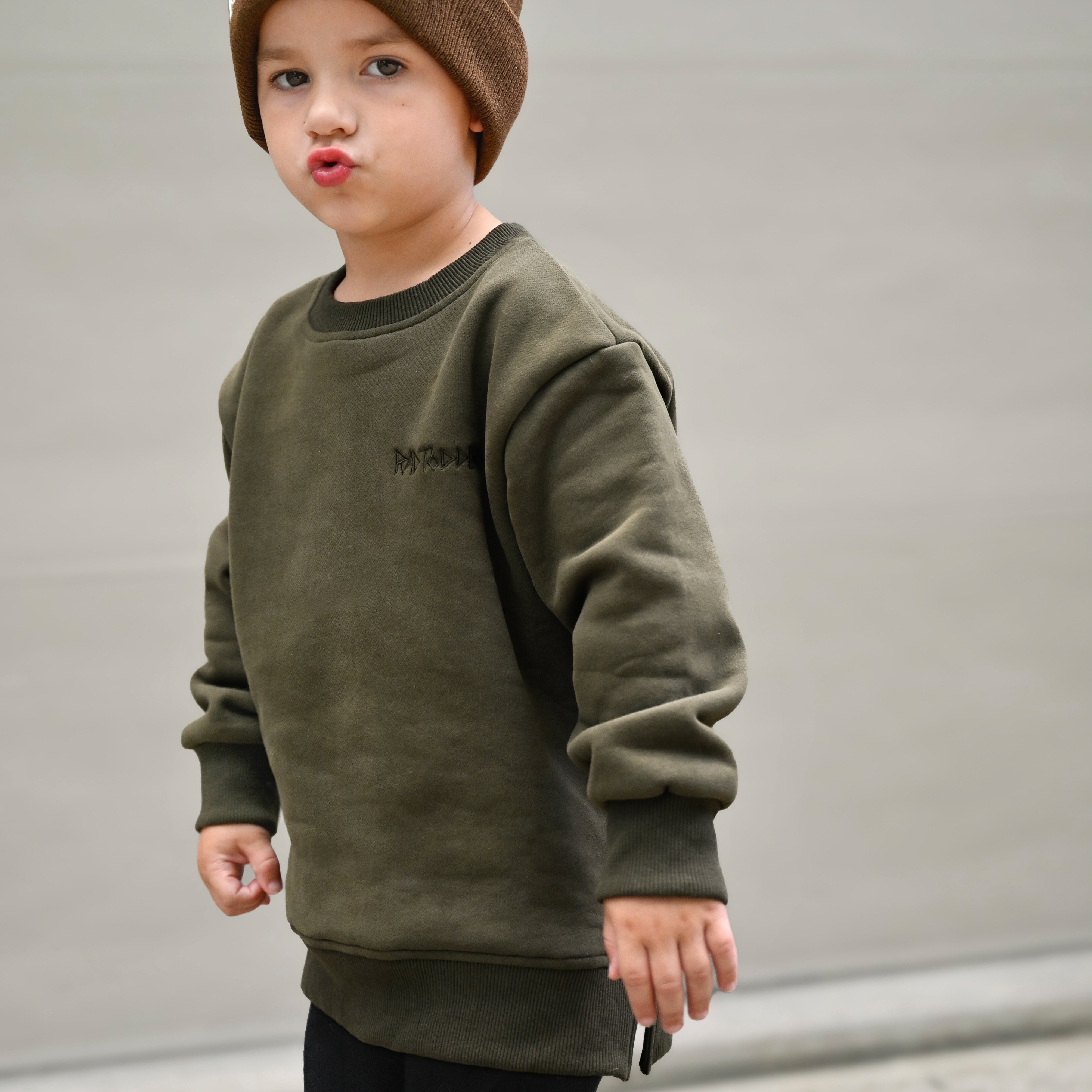Young boy in Flaming Fast crewneck playing outdoors, showcasing dark green sweatshirt with skull graphic