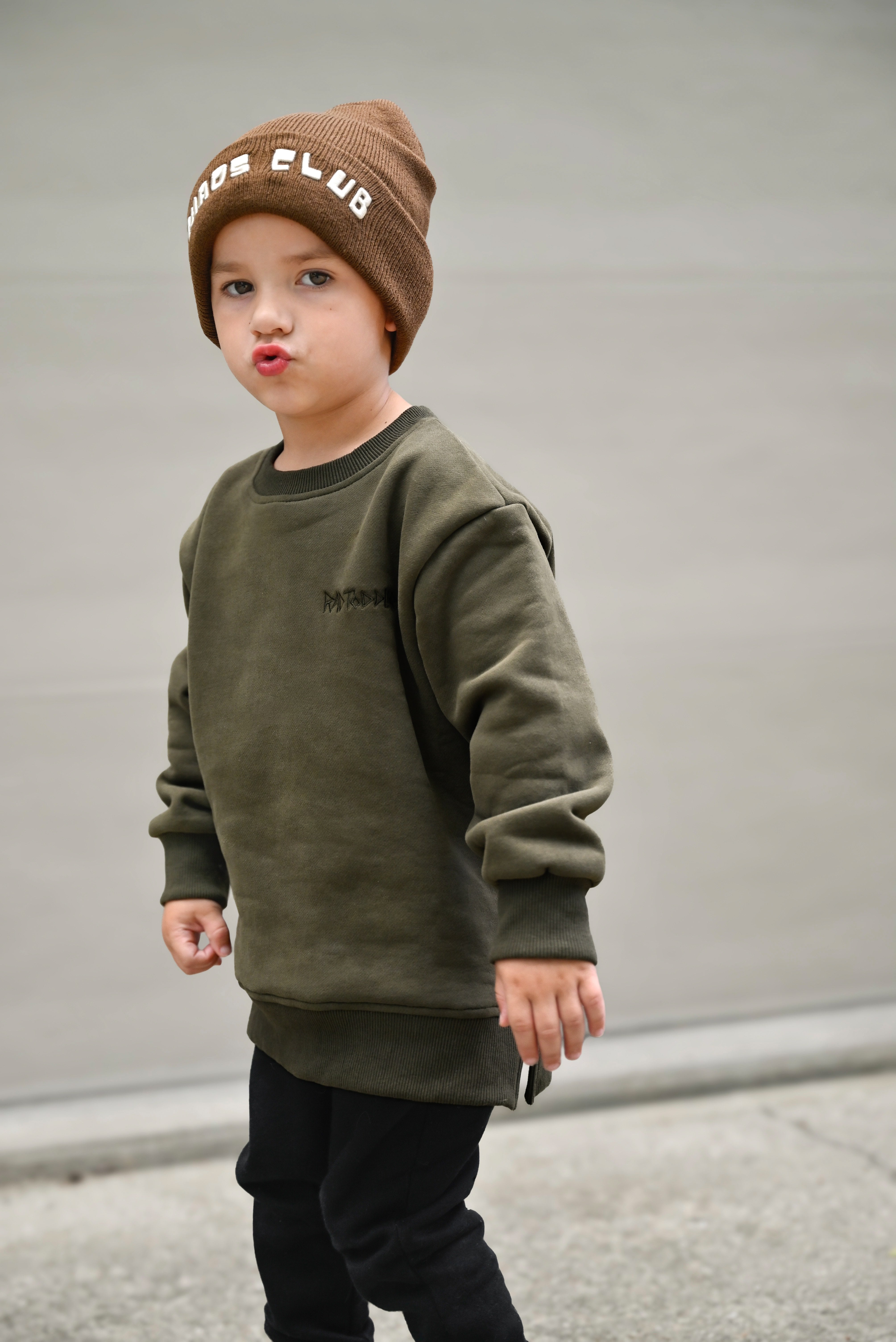 Young boy in Flaming Fast crewneck playing outdoors, showcasing dark green sweatshirt with skull graphic