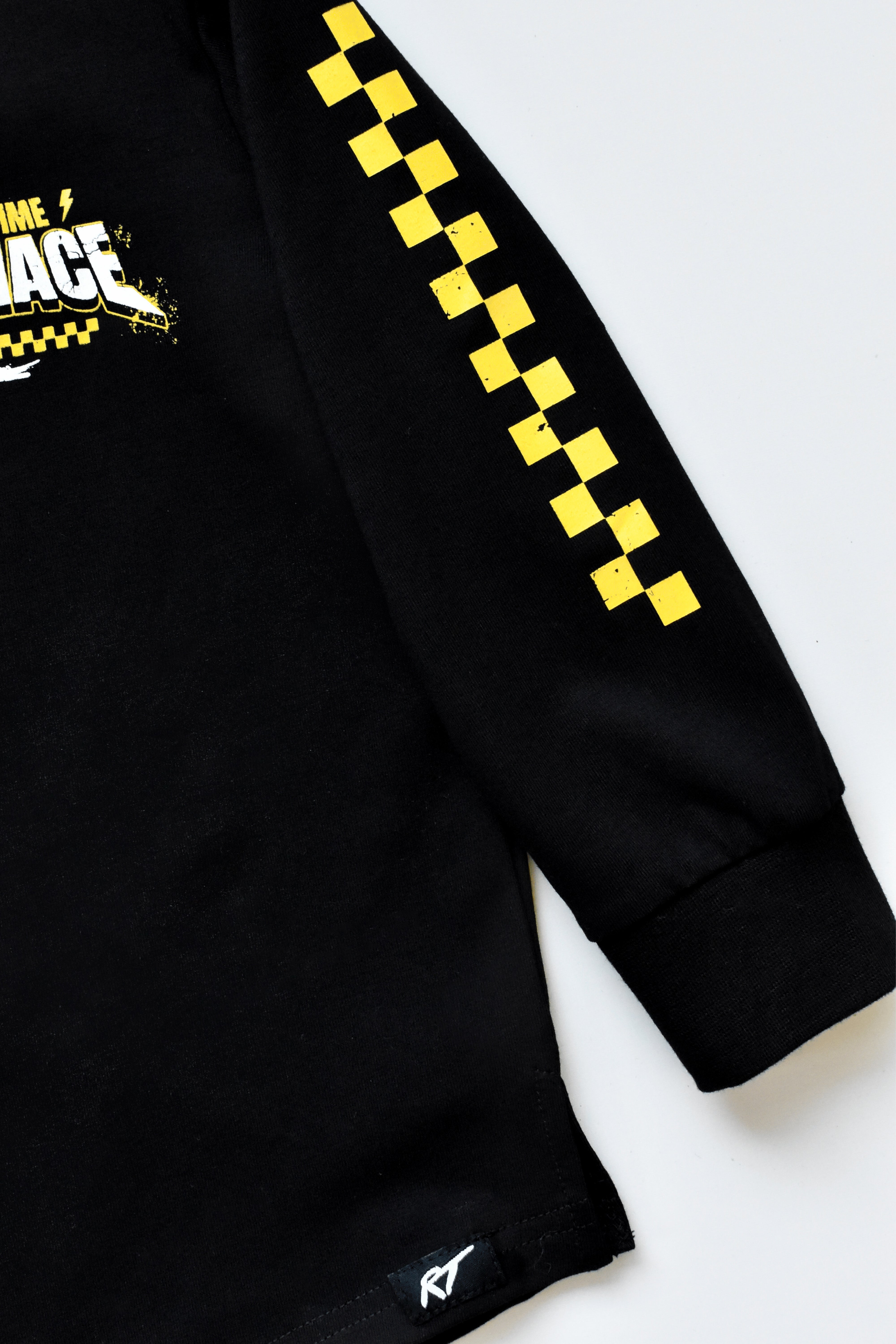 Close-up of a black long-sleeve shirt with a yellow and black checkered pattern down one sleeve and a partial graphic on the chest, shown on a light gray background.