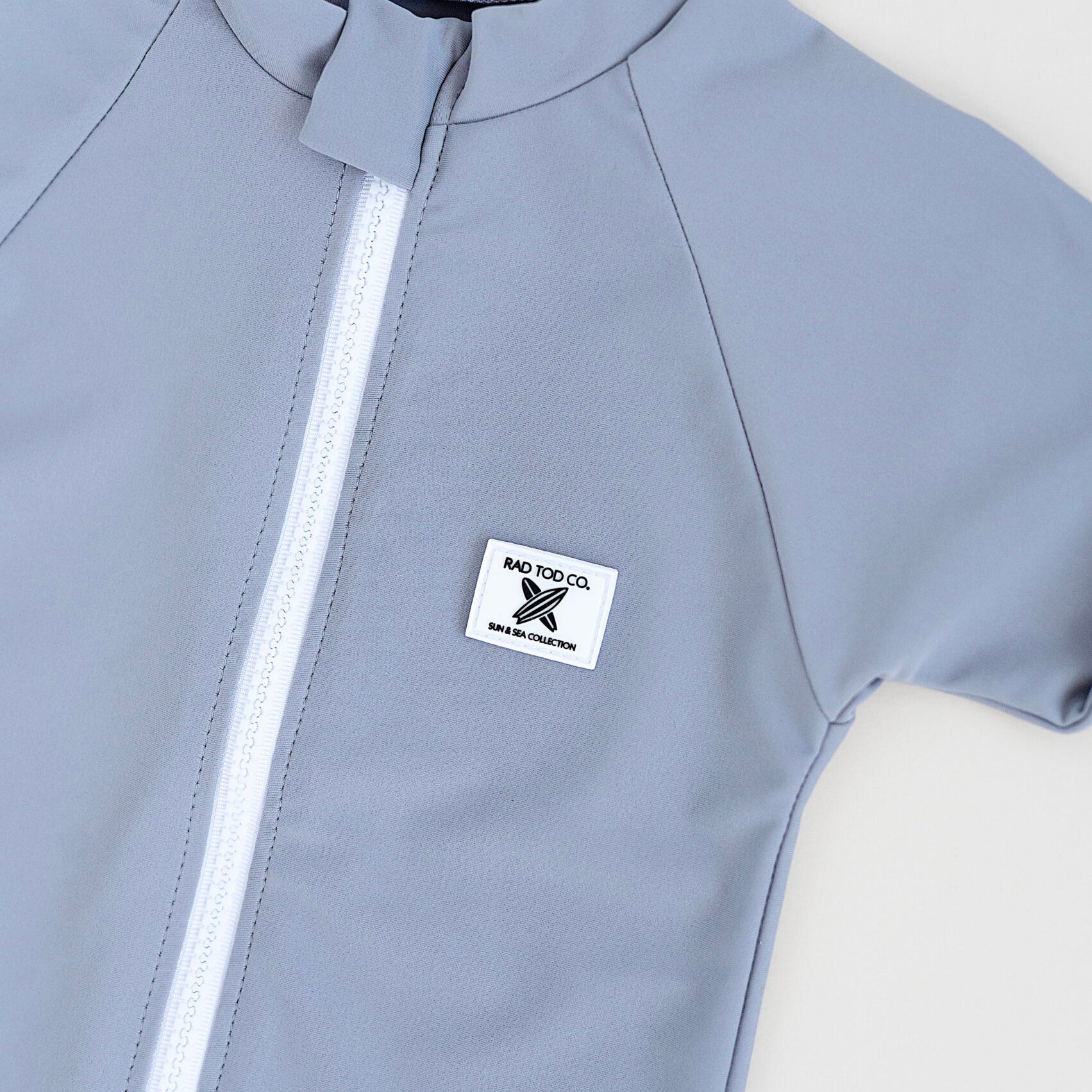 details on Rad Toddlers gray Rashguard Shirt with front zipper and UPF 50+ protection, perfect for pairing with board shorts for water activities.