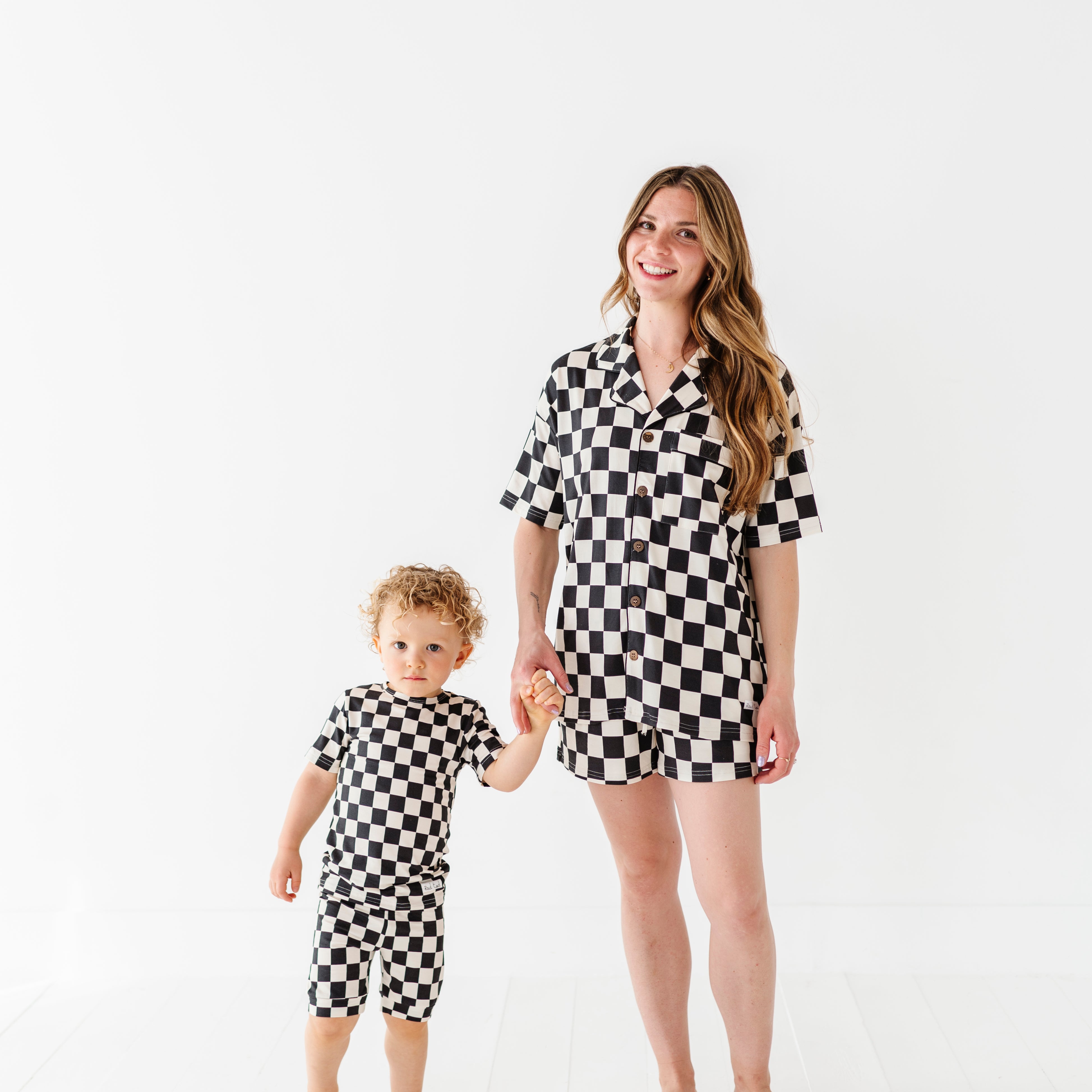 hand in hand wearing Black and white checkered bamboo short sleeve pajama set for women, featuring soft, breathable fabric and a relaxed fit by Rad Toddler.