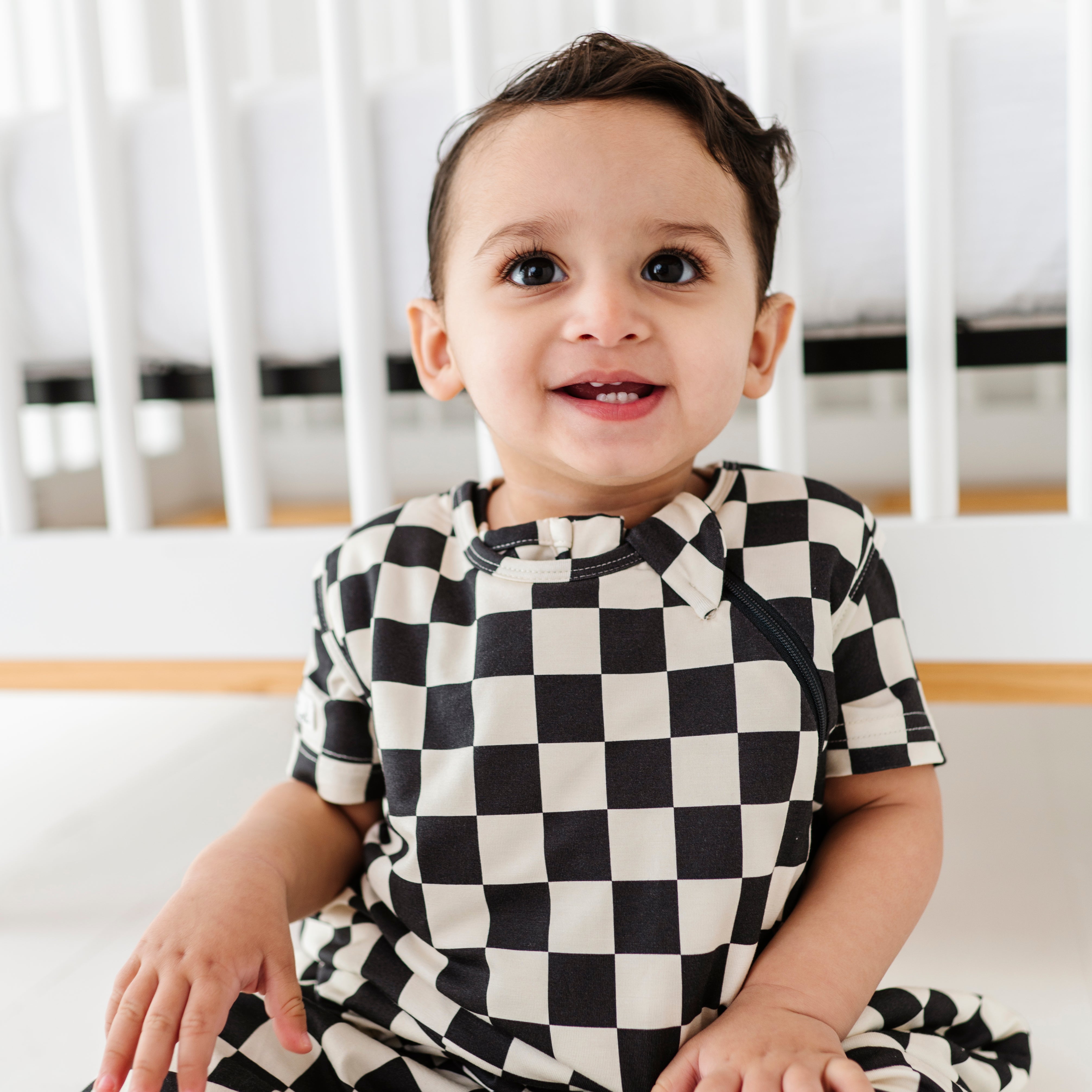 boy smiling wearing Bamboo sleep bag for toddlers in black and white checkered pattern, featuring a two-way zipper by Rad Toddler.