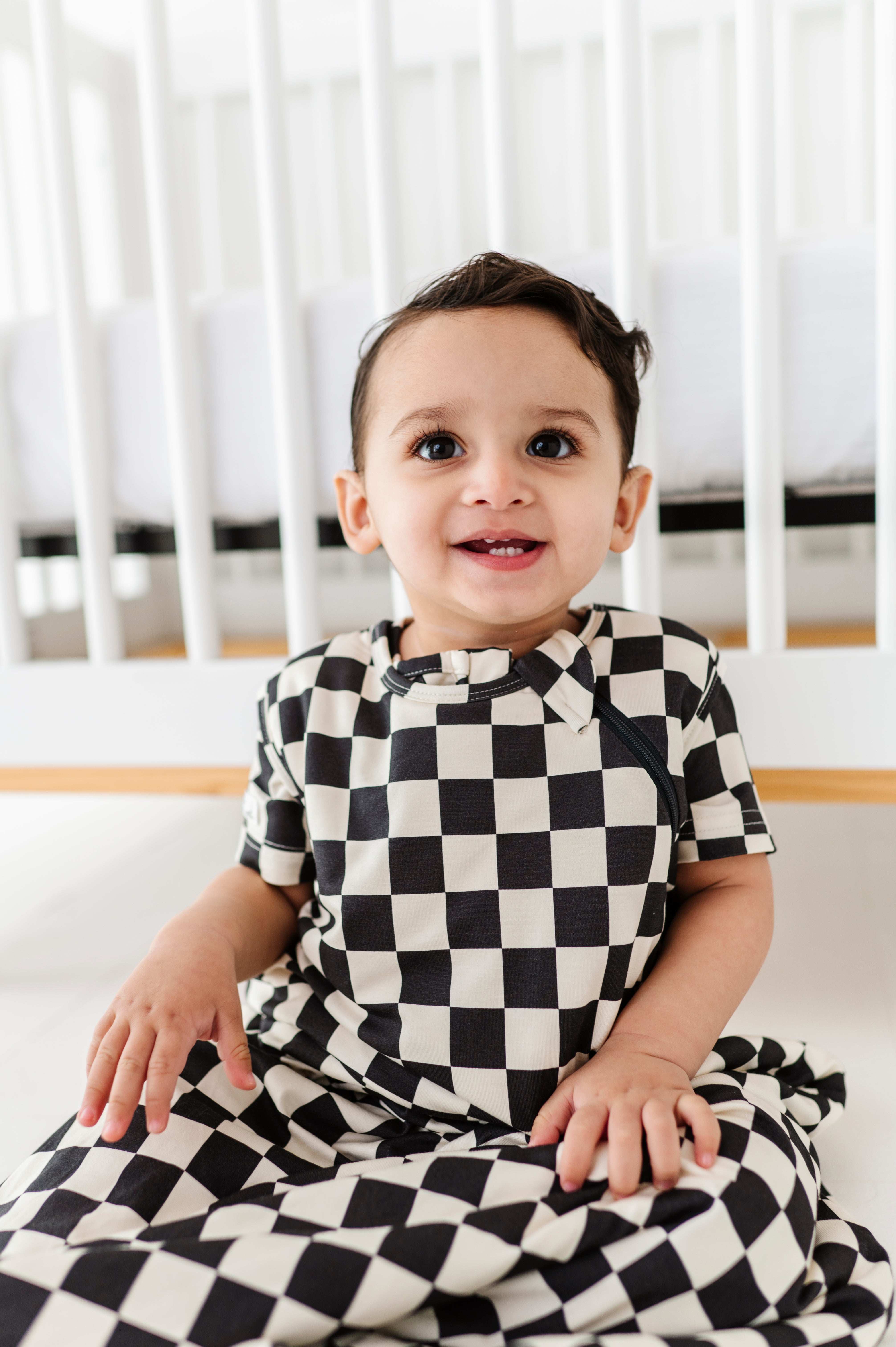 boy smiling wearing Bamboo sleep bag for toddlers in black and white checkered pattern, featuring a two-way zipper by Rad Toddler.