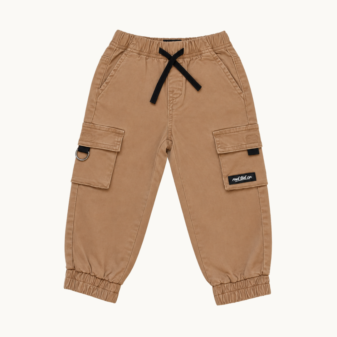 A pair of toddler cargo pants in tan, featuring a black drawstring waist, elastic cuffs, and side cargo pockets, shown against a plain off-white background.