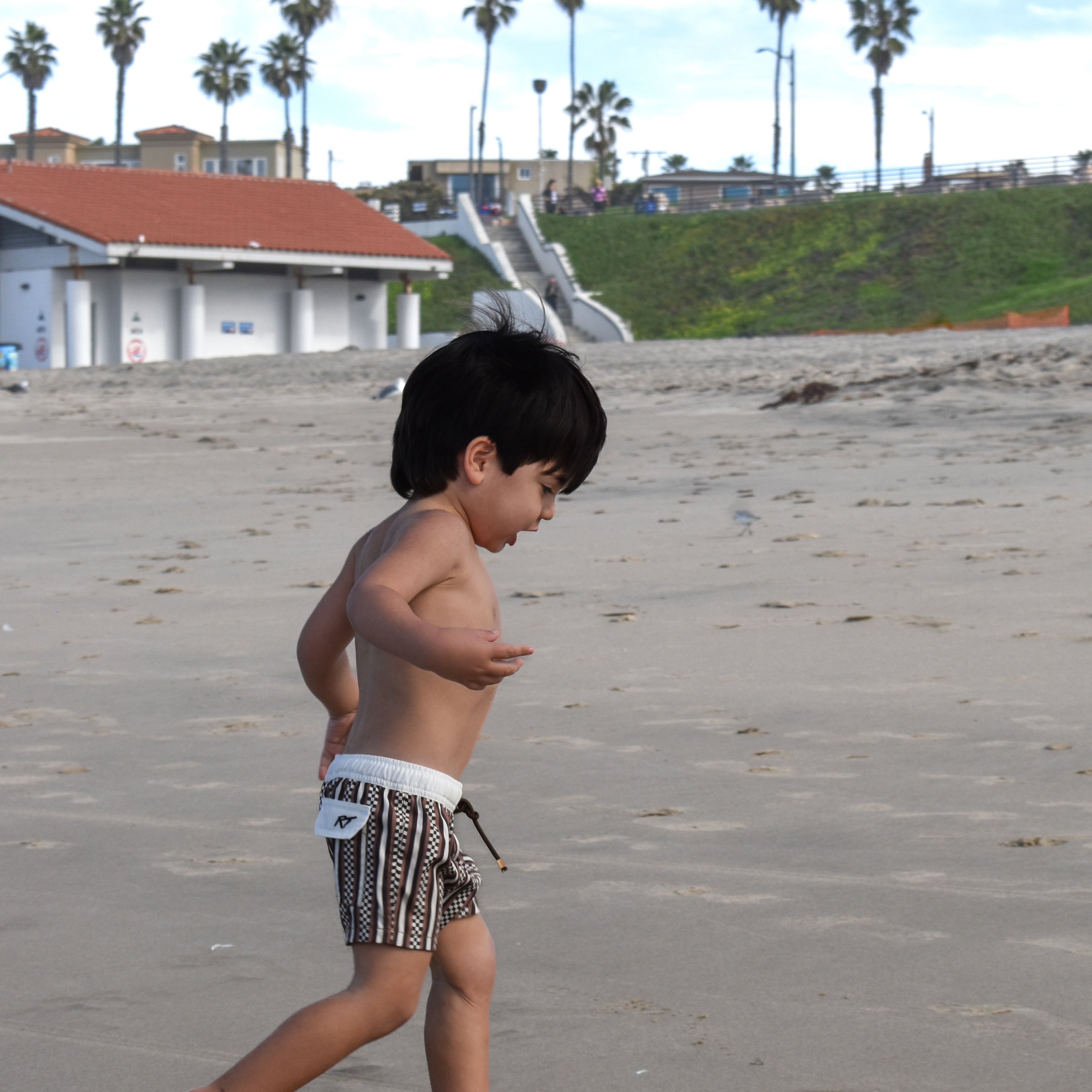 Child wearing Latte Stripes Swimmie with warm coffee-tone stripes while running on a beach