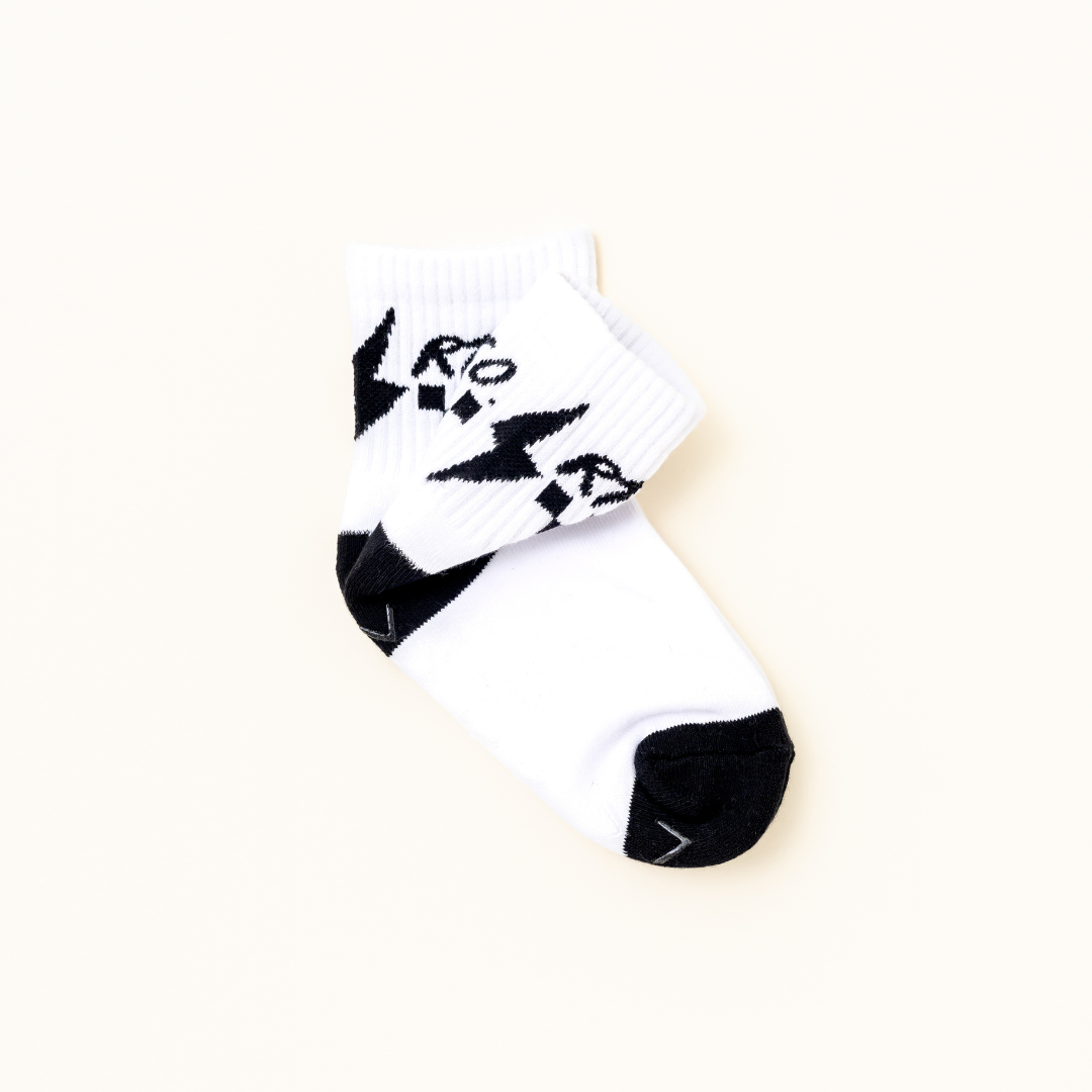 A pair of white ankle socks with black accents on the toe, heel, and cuff, featuring a black graphic pattern and the brand name 'RT co' printed on the cuff, set against a solid off-white background.