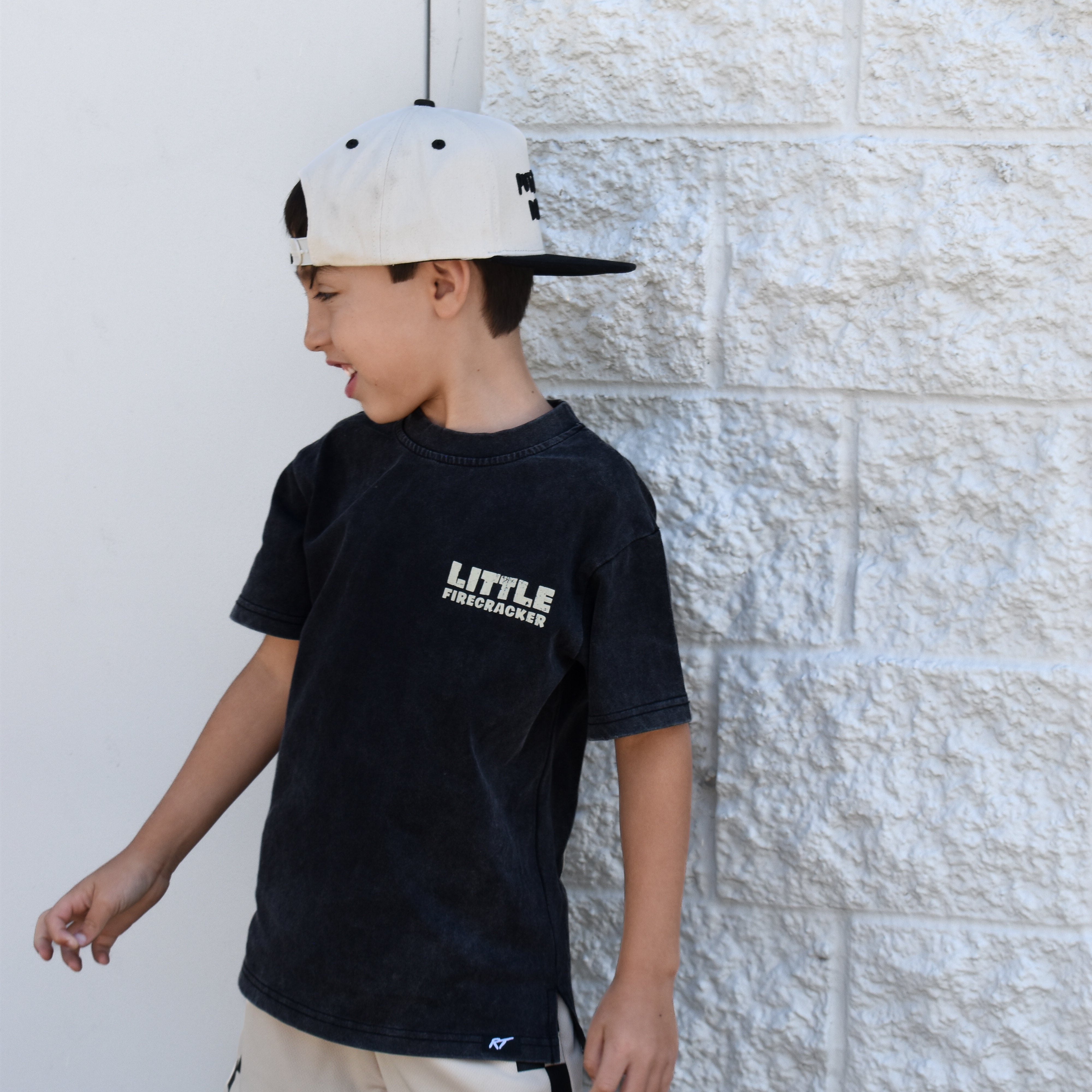 Kid wearing the Little Firecracker graphic tee on a black acid wash shirt with patriotic red, white, and blue design.