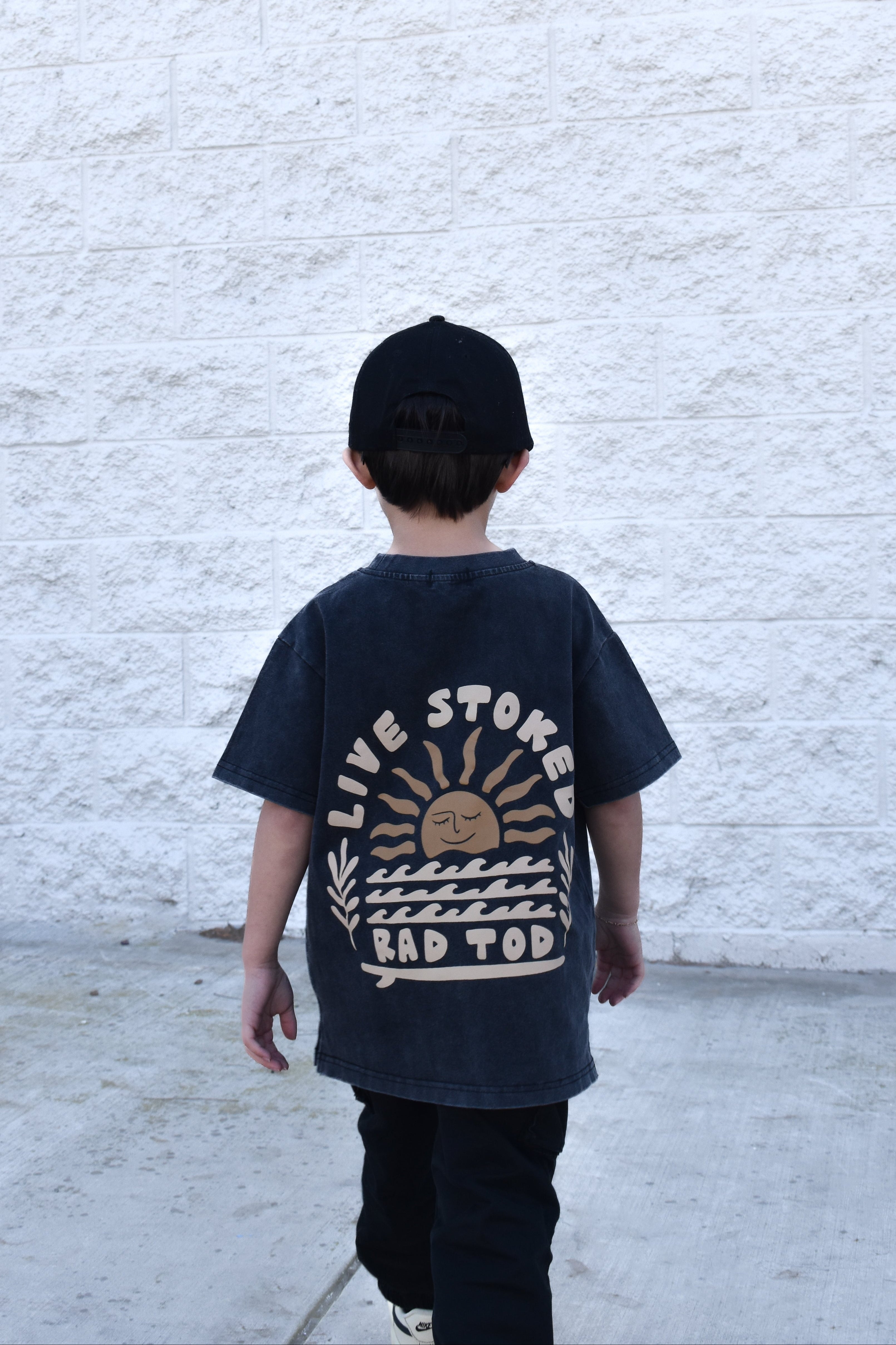 Kid wearing Live Stoked black acid wash t-shirt with golden sun and surfboard design