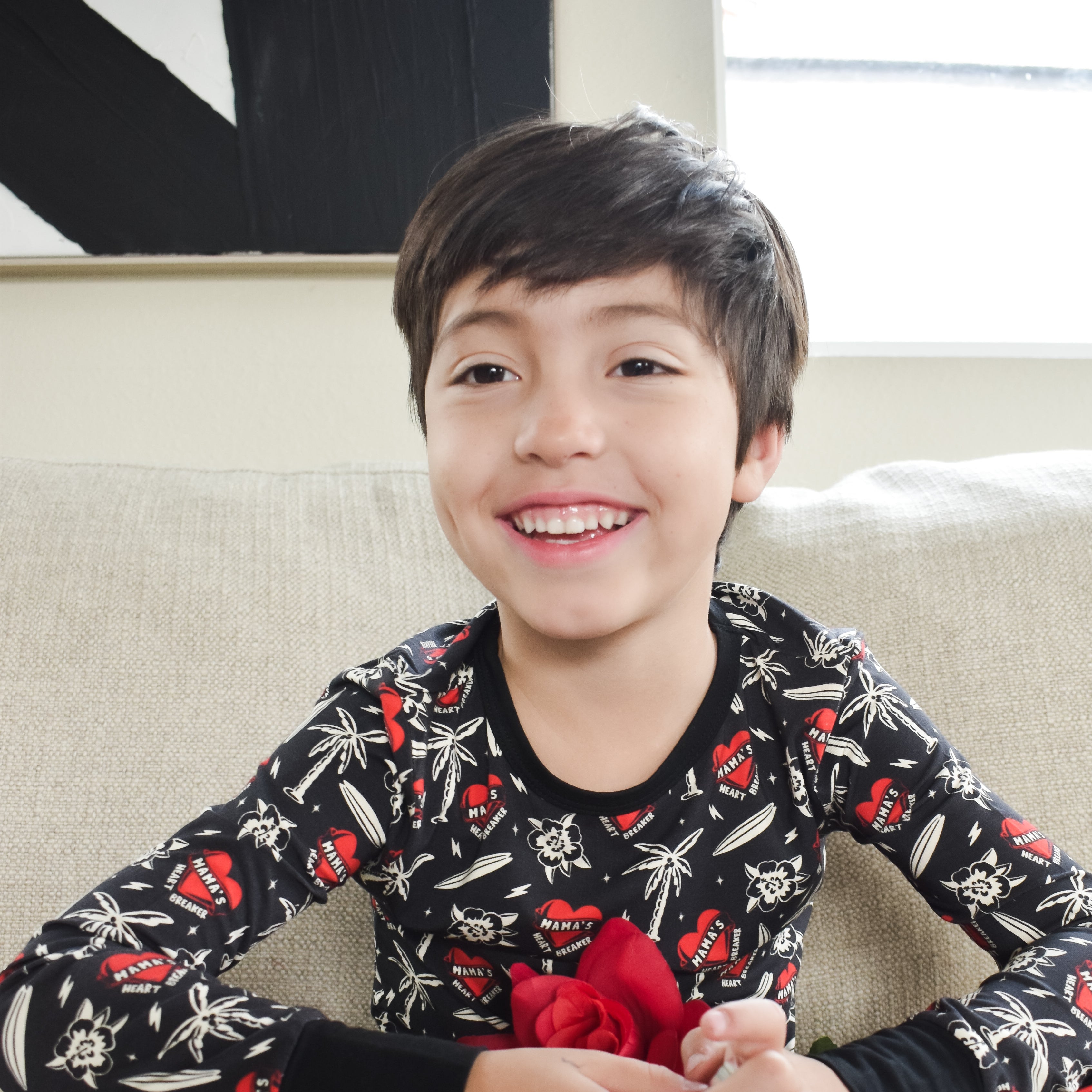 Child wearing a black pajama set with red flowers sitting on a couch.