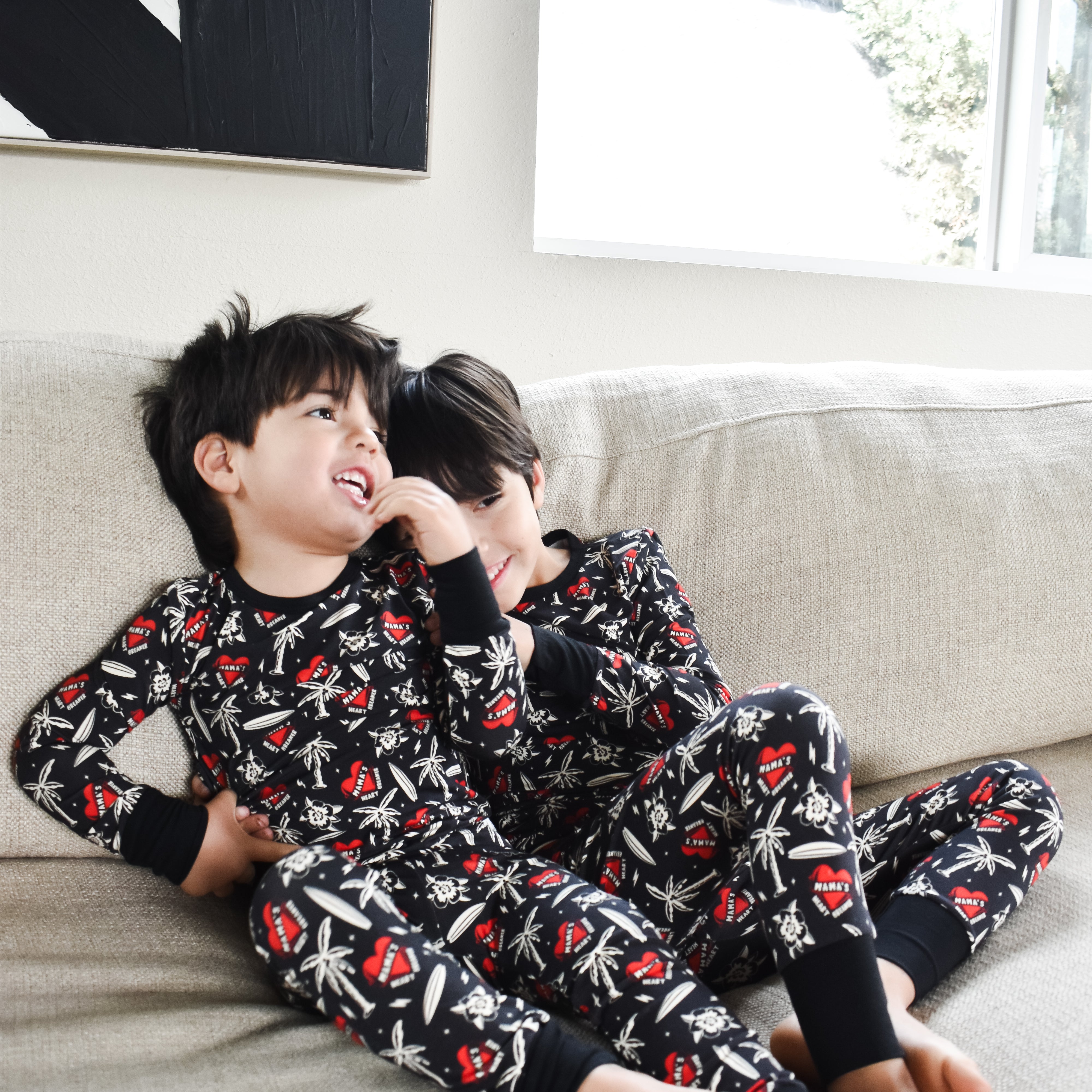 Two children in matching pajamas sitting on a couch in a living room in mamas heartbreaker pajamas by rad toddler