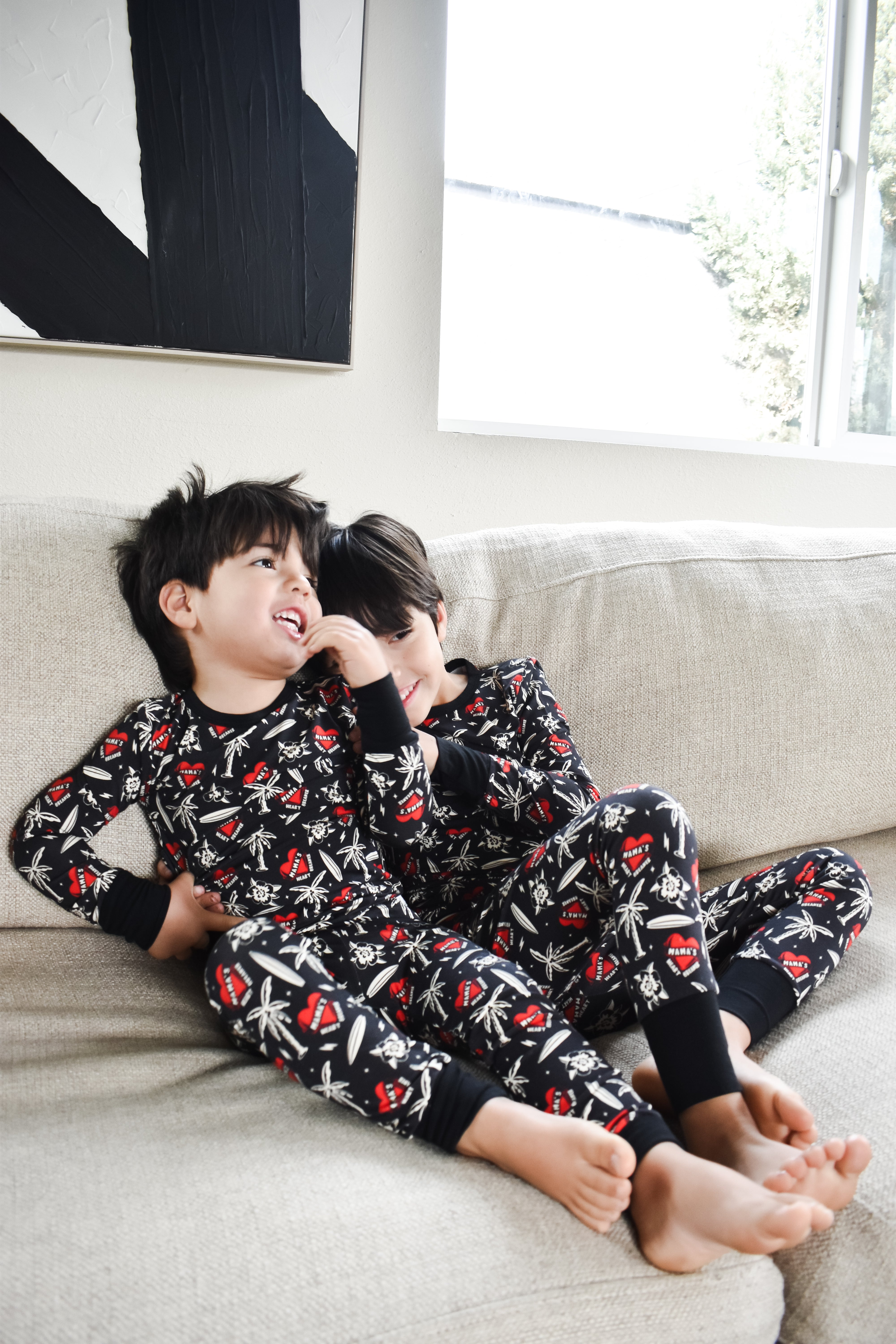 Two children in matching pajamas sitting on a couch in a living room in mamas heartbreaker pajamas by rad toddler