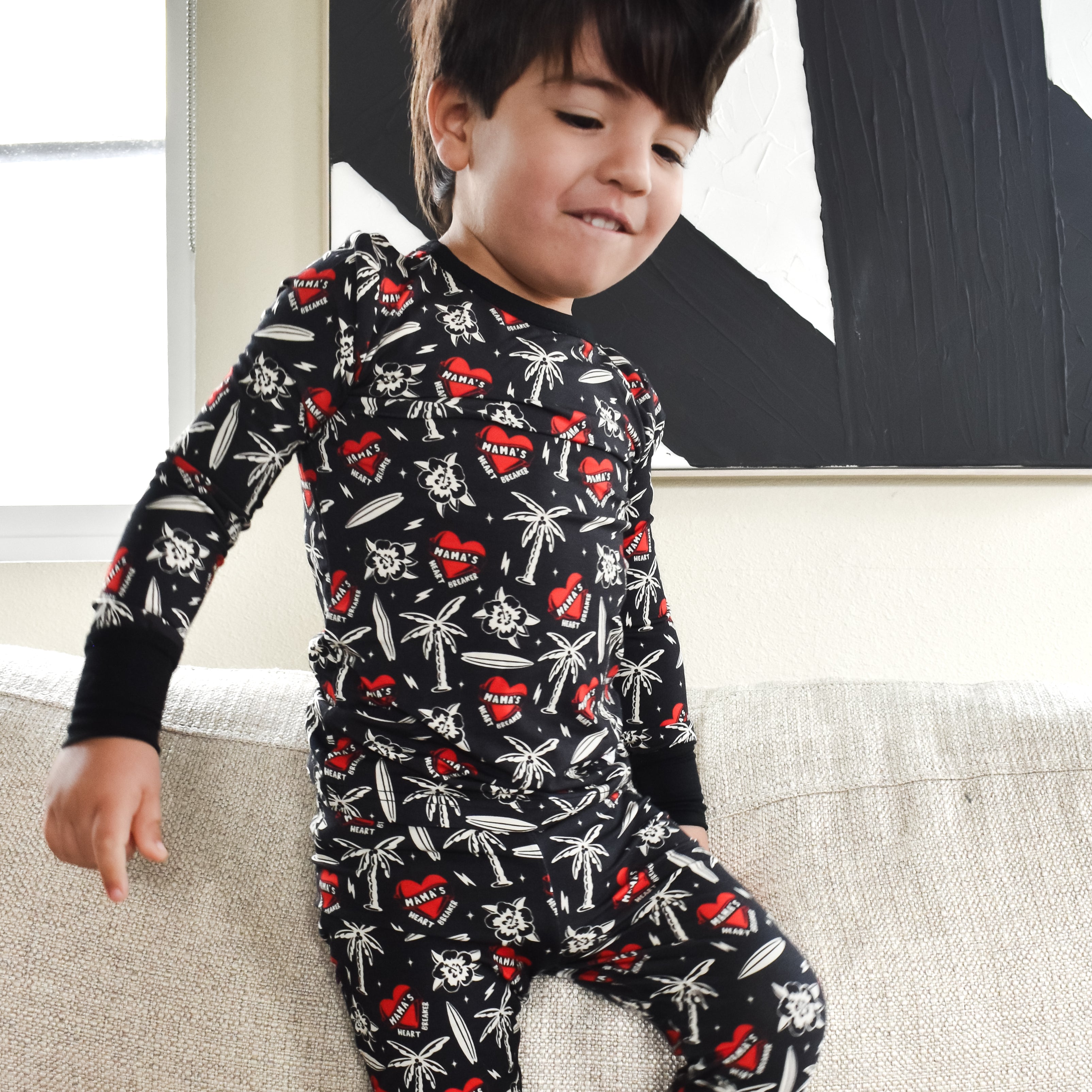 Child wearing a black pajama set with red and white patterns on a beige couch.
