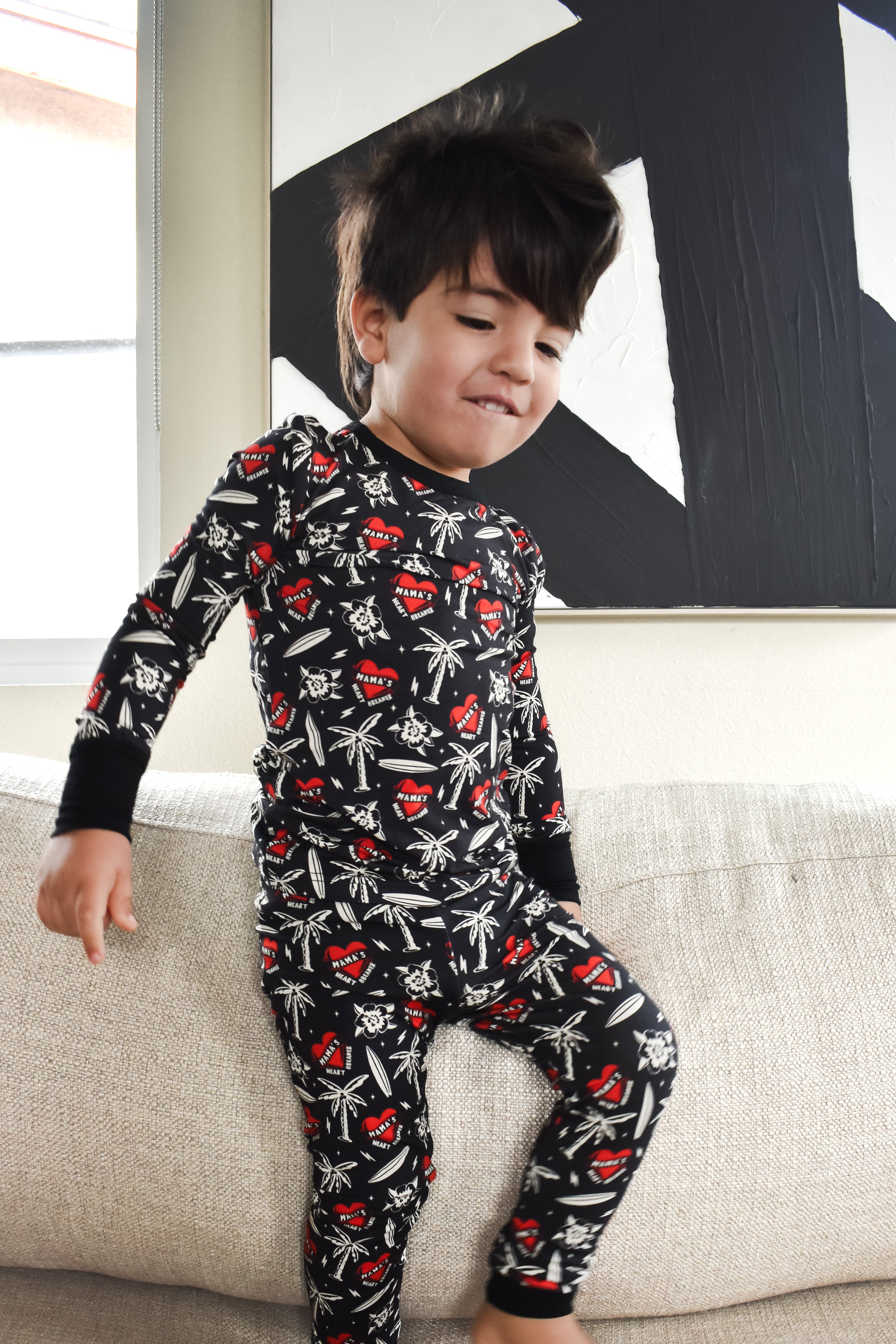 Child wearing a black pajama set with red and white patterns on a beige couch.