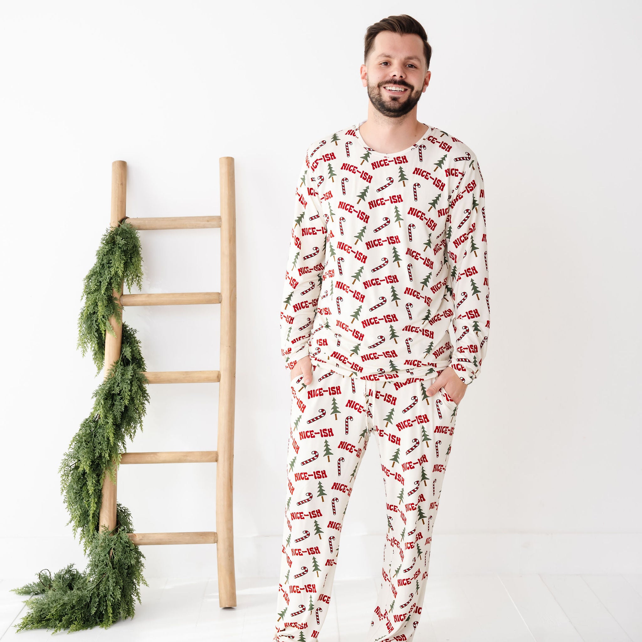 Man wearing a festive pajama set with a ladder and greenery on a white background