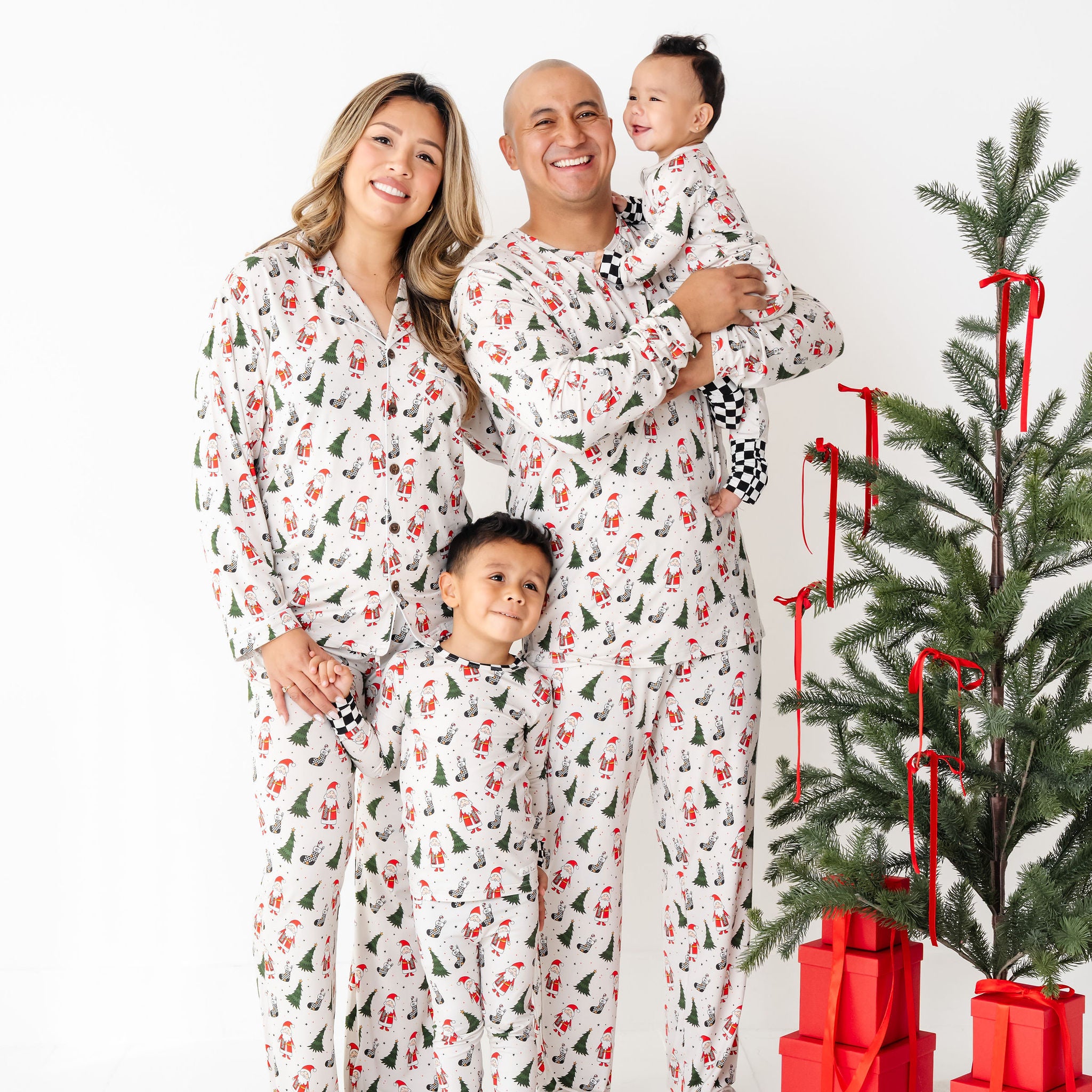 Family in matching pajamas standing next to a decorated Christmas tree with red presents.