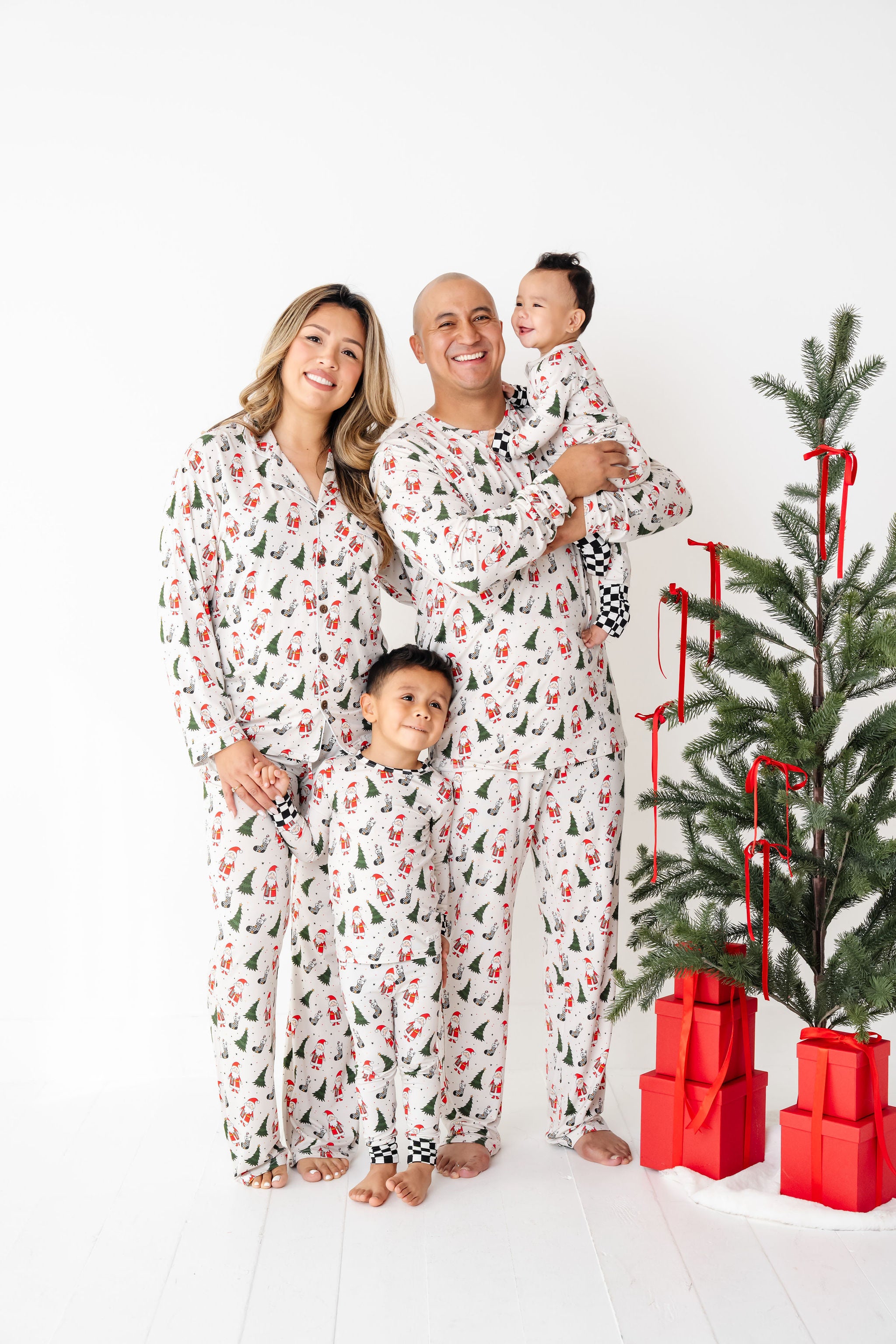 Family in matching pajamas standing next to a decorated Christmas tree with red presents.