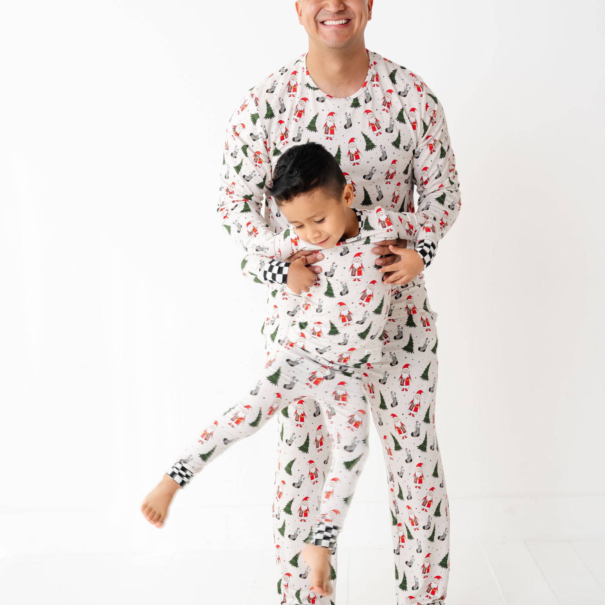 Man and child wearing matching pajamas by Rad toddler called Merry Everything Bamboo Christmas Pajamas with Santa, trees, and checkered stockings