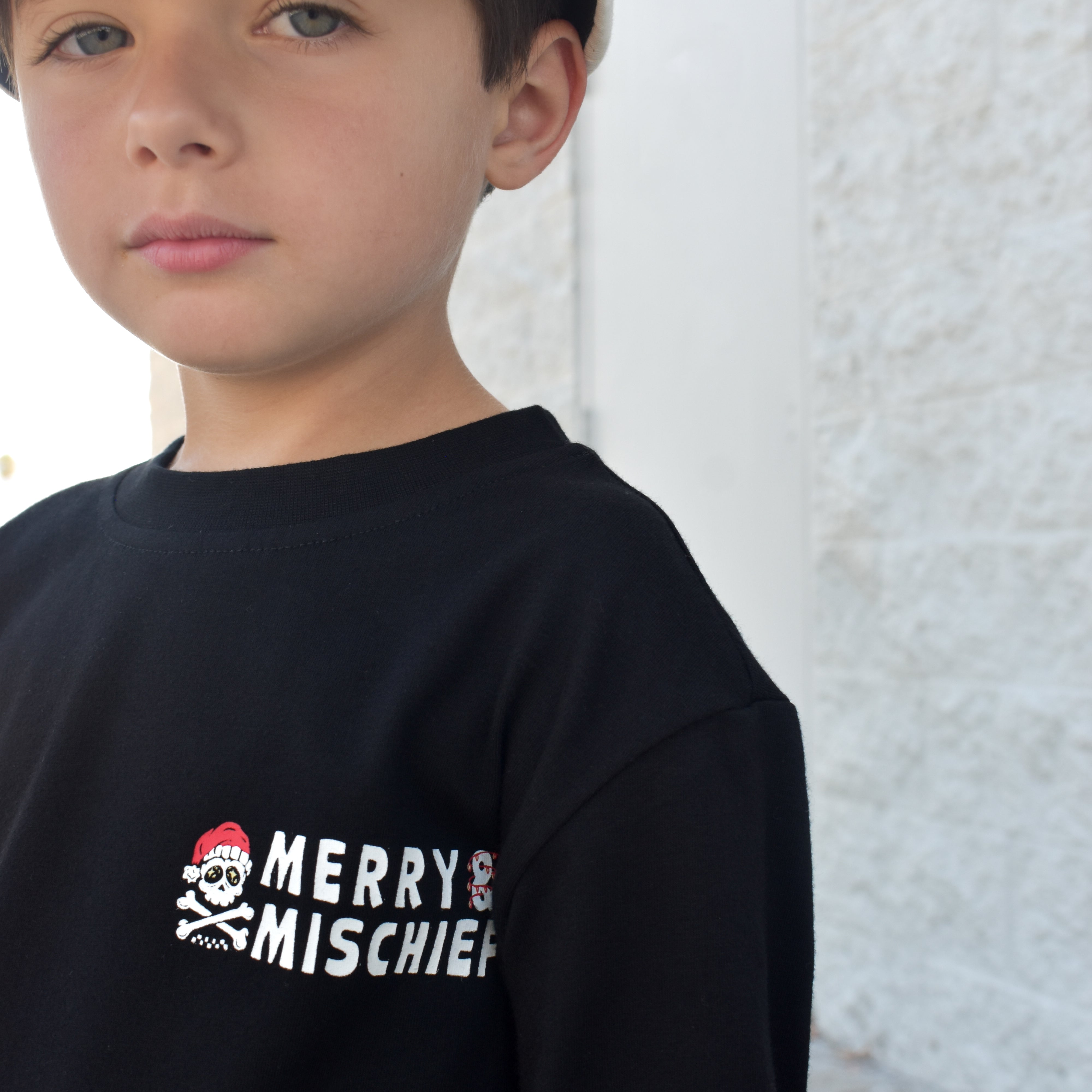 Child wearing a black sweatshirt with 'Merry Mischief' text and skull design.