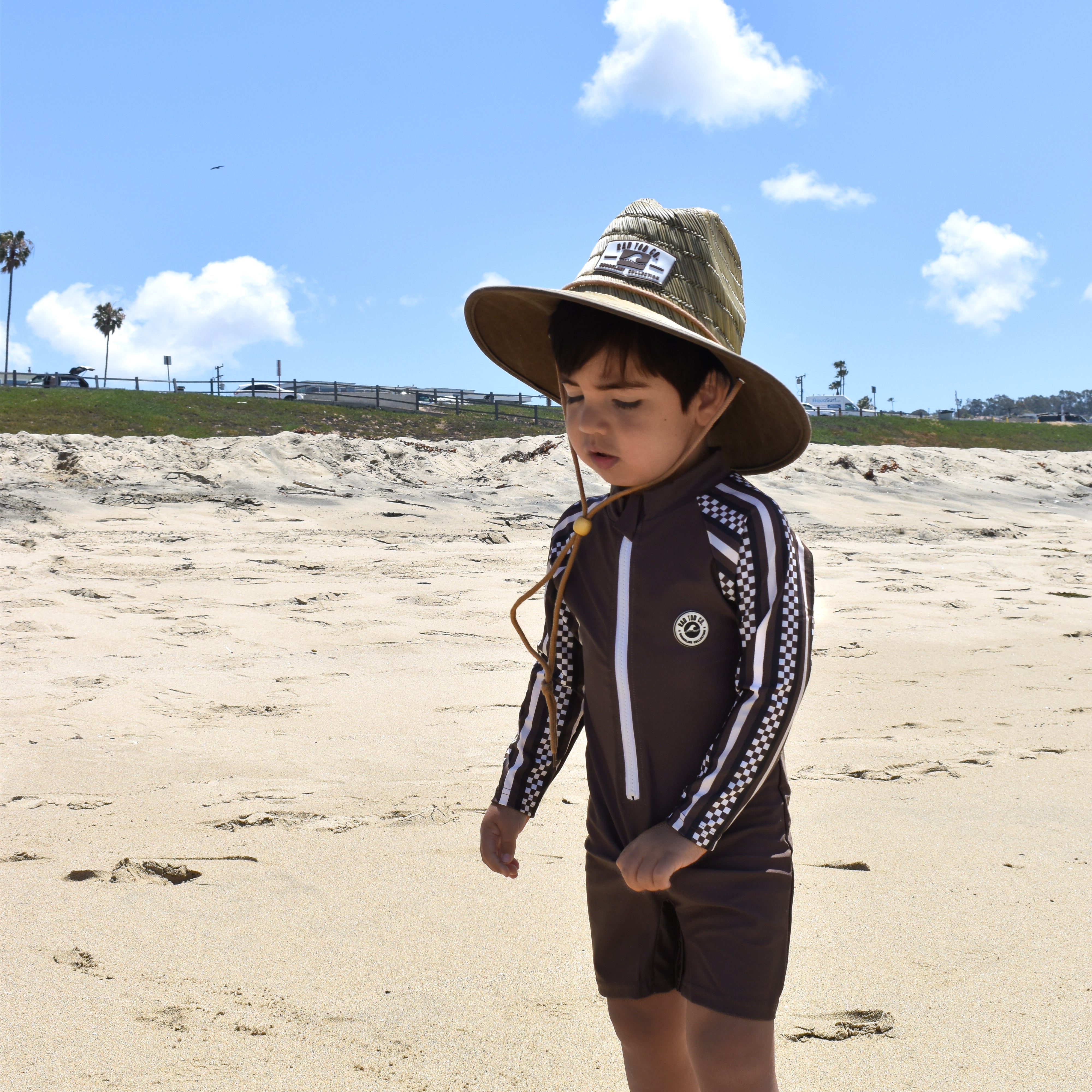 Child wearing a hat and swimsuit on a sandy beach with a clear blue sky.