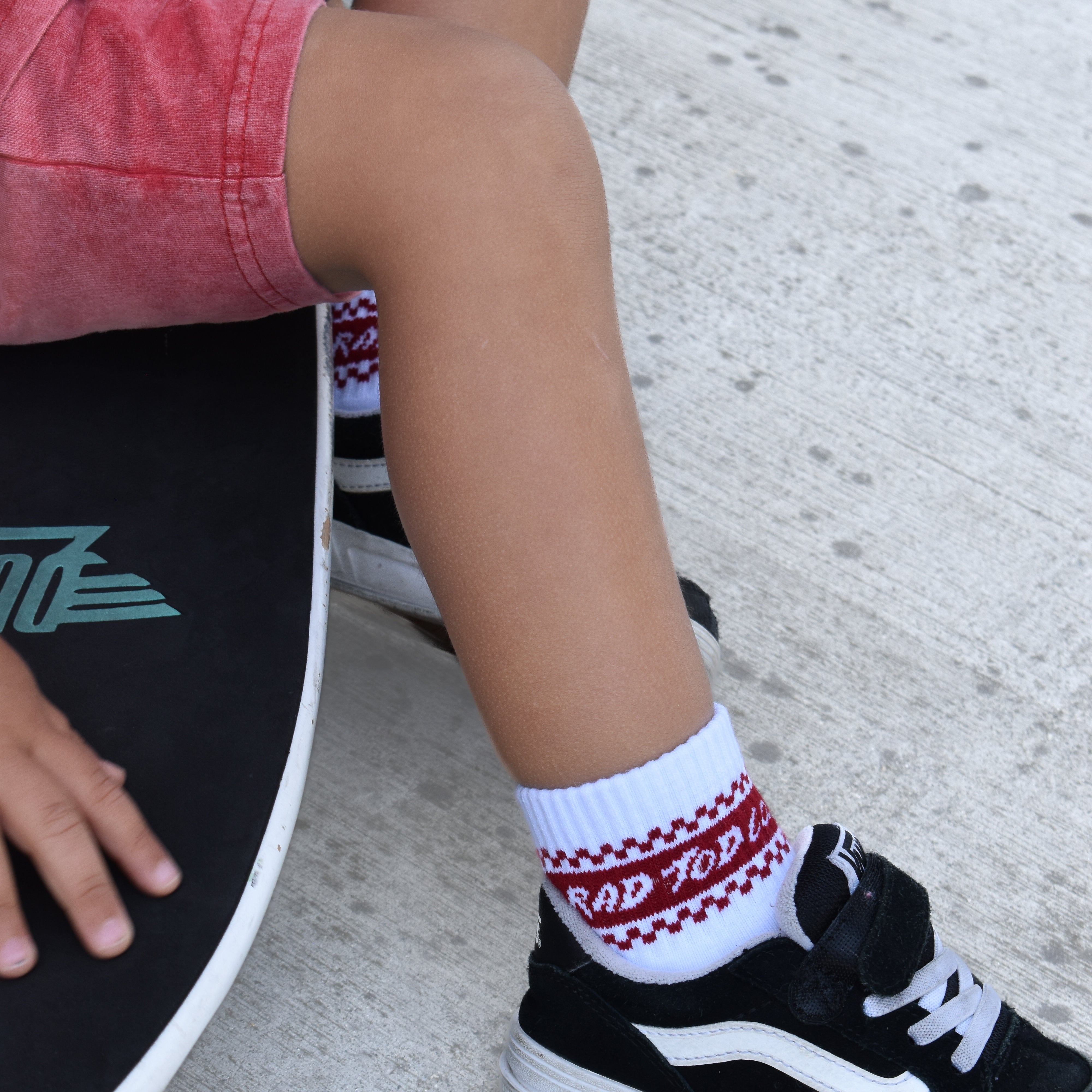 Person wearing a black shoe with white laces and a red and white checkered sock, sitting on a skateboard.