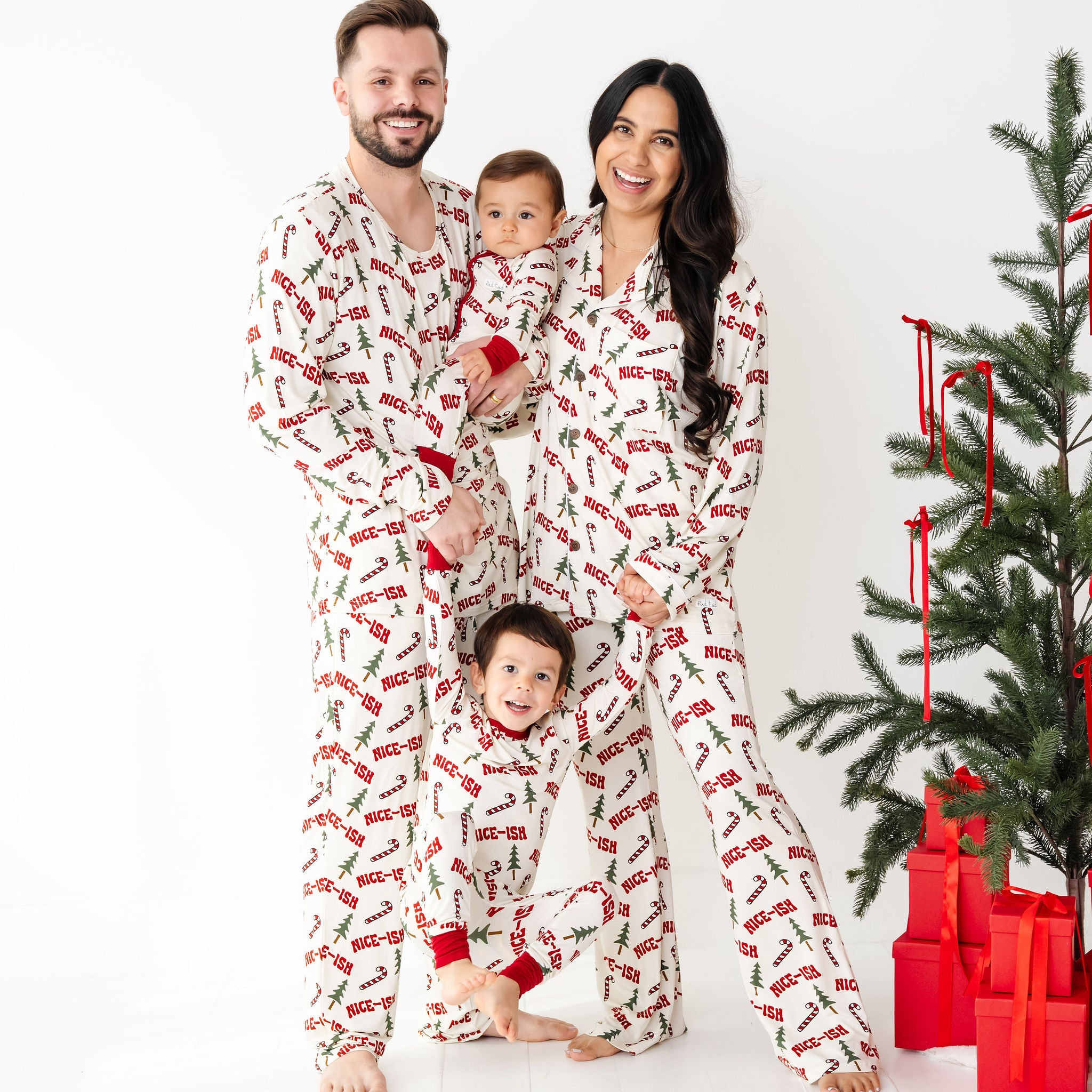 Family of four wearing matching pajamas in front of a Christmas tree with presents. They are wearing Nice-ish bamboo which is white and the writing is in RED