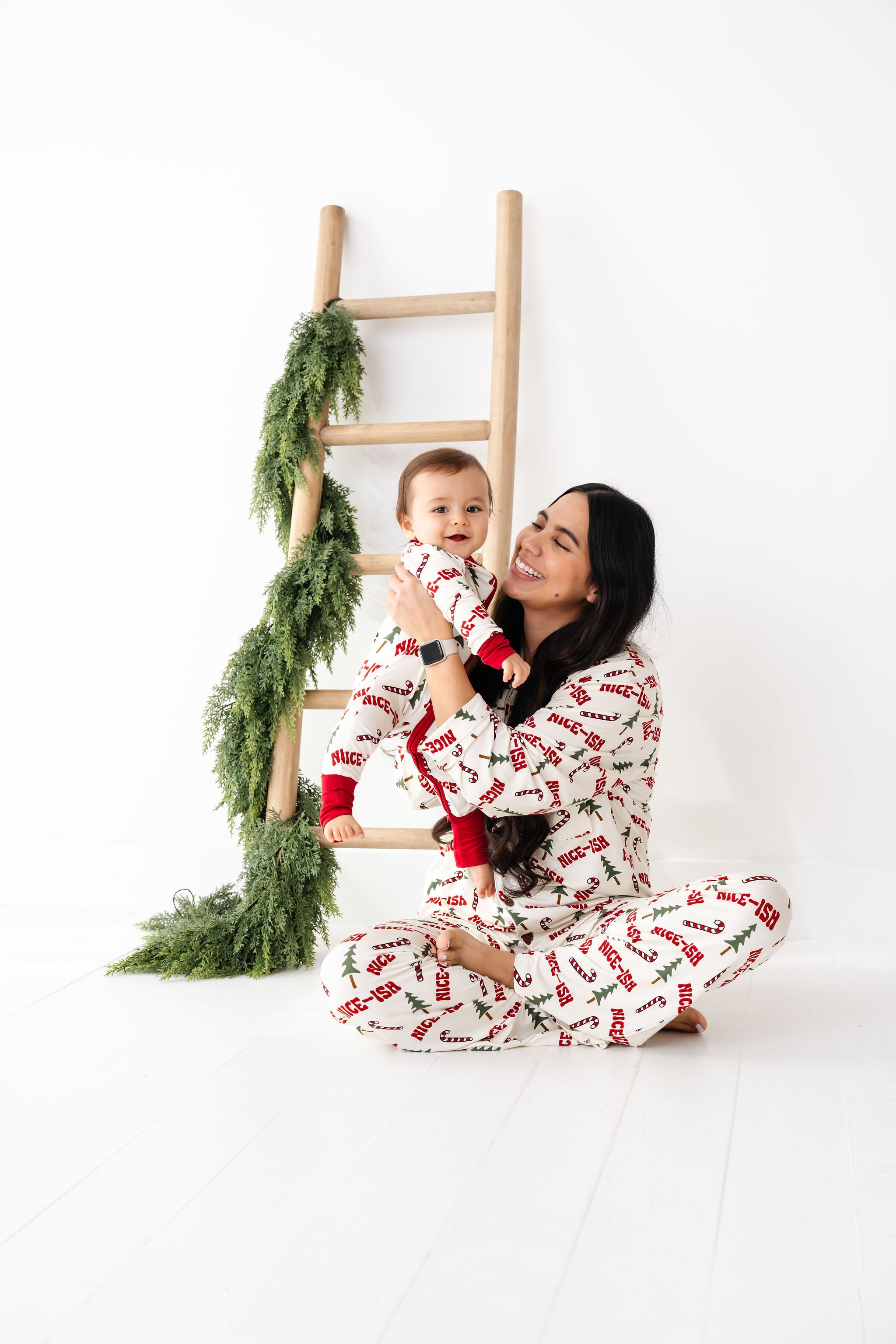 Woman and child in matching pajamas sitting on a ladder with Christmas decorations.