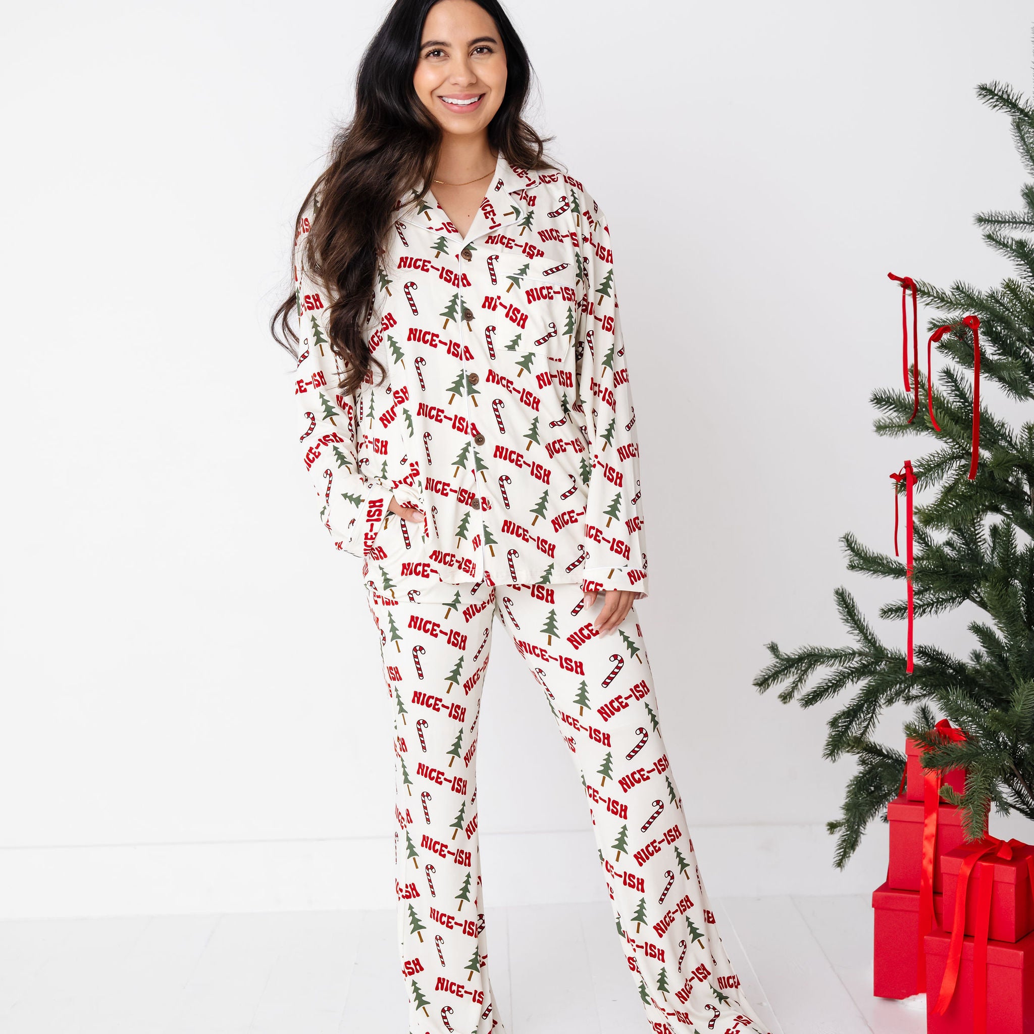 Woman wearing a festive pajama set with a Christmas tree and presents in the background.