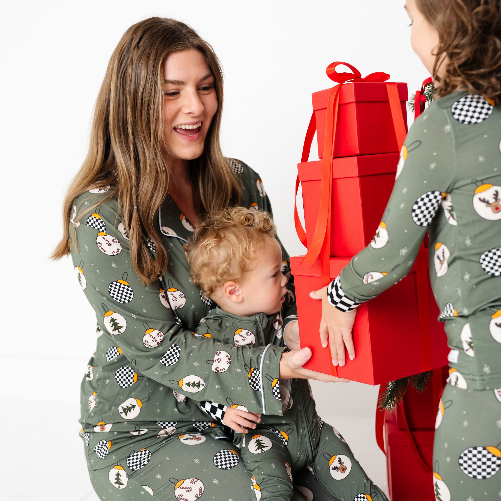 Woman and two children in matching pajamas with a red gift box on a white background