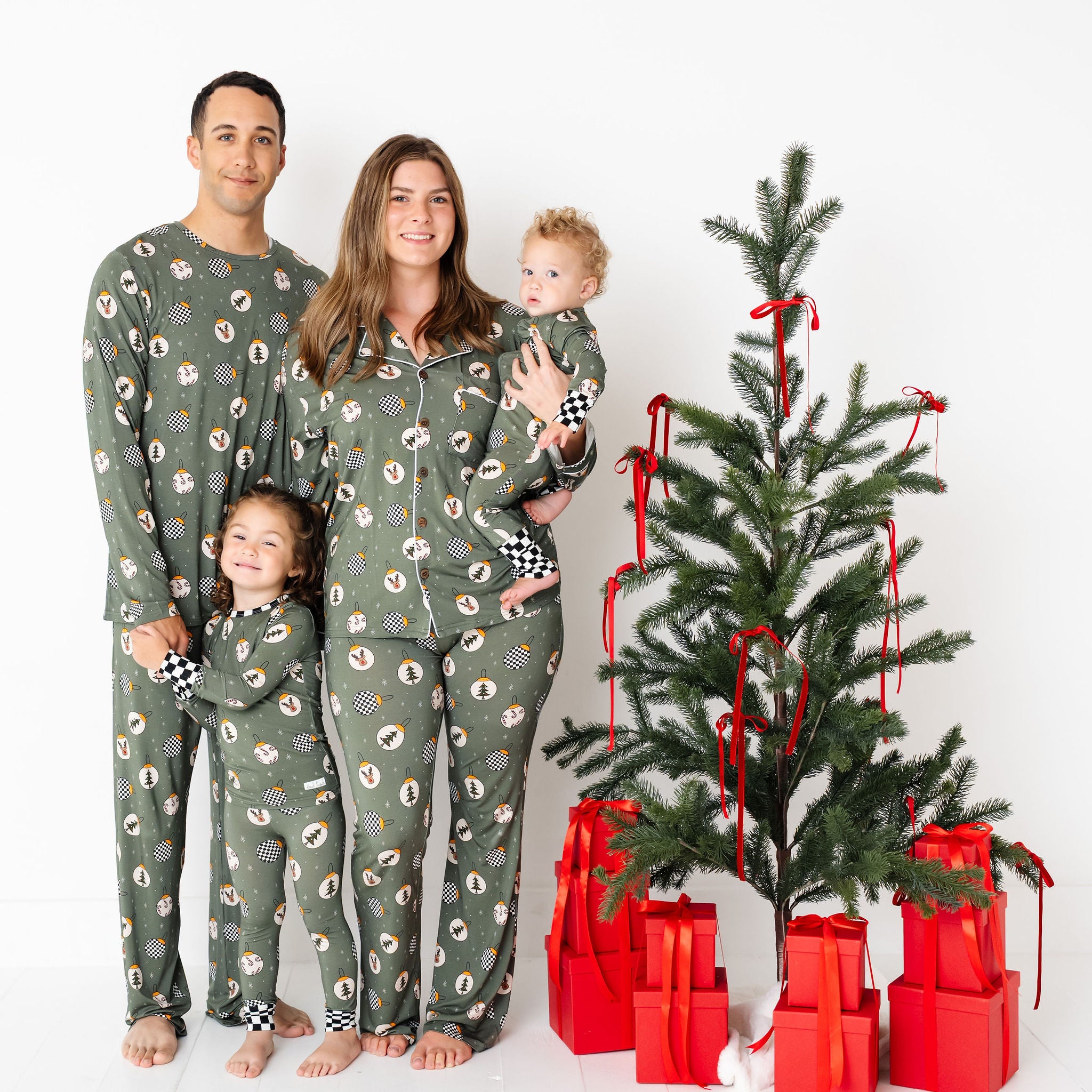 Family in matching green pajamas with a Christmas tree and presents on a white background