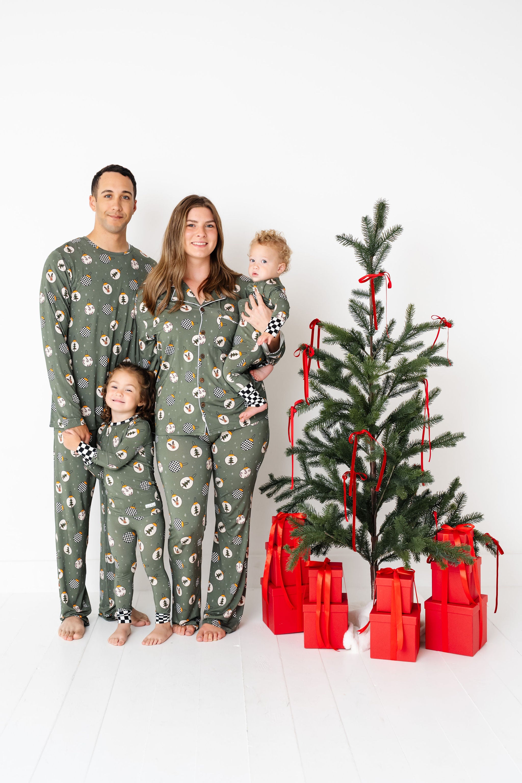 Family in matching green pajamas with a Christmas tree and presents on a white background