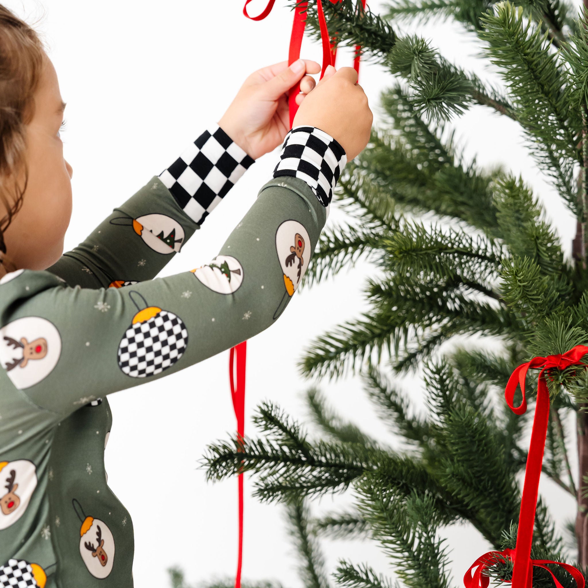 Child decorating a Christmas tree with red ribbons