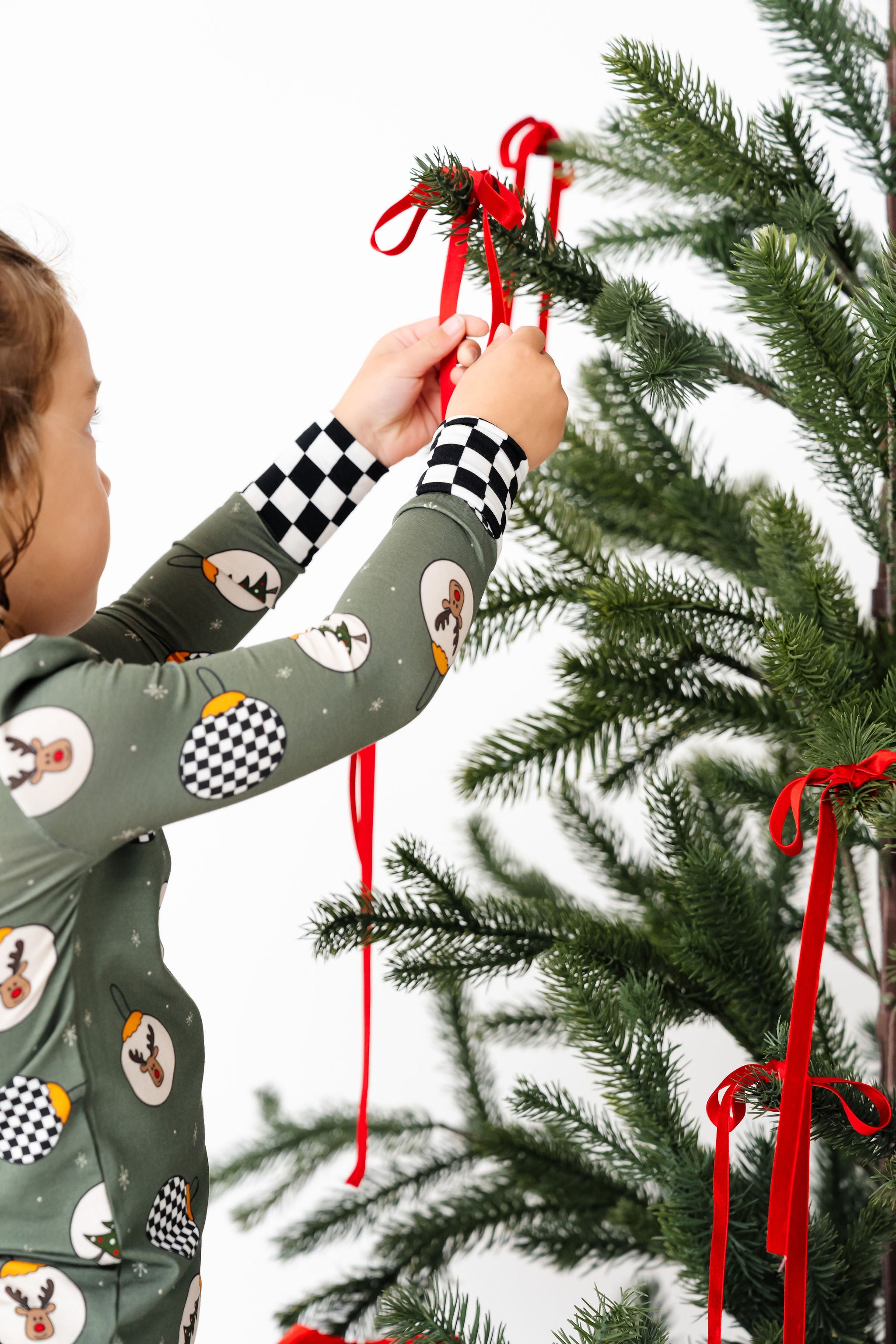 Child decorating a Christmas tree with red ribbons
