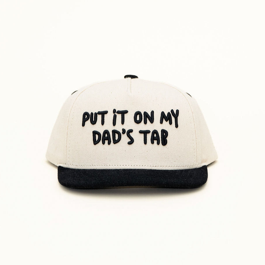 Front view of Put It On My Dad’s Tab kids snapback with playful embroidery on off-white crown and black bill.