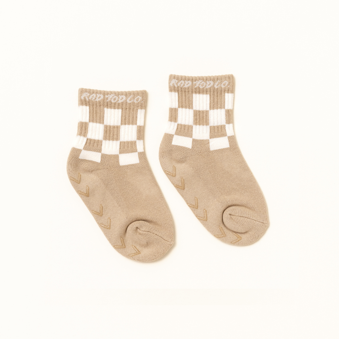 A pair of beige ankle socks with white checkered patterns on the upper cuff and textured grip dots on the sole, featuring the brand name 'RAD TOD CO' printed in white on the ribbed cuffs.