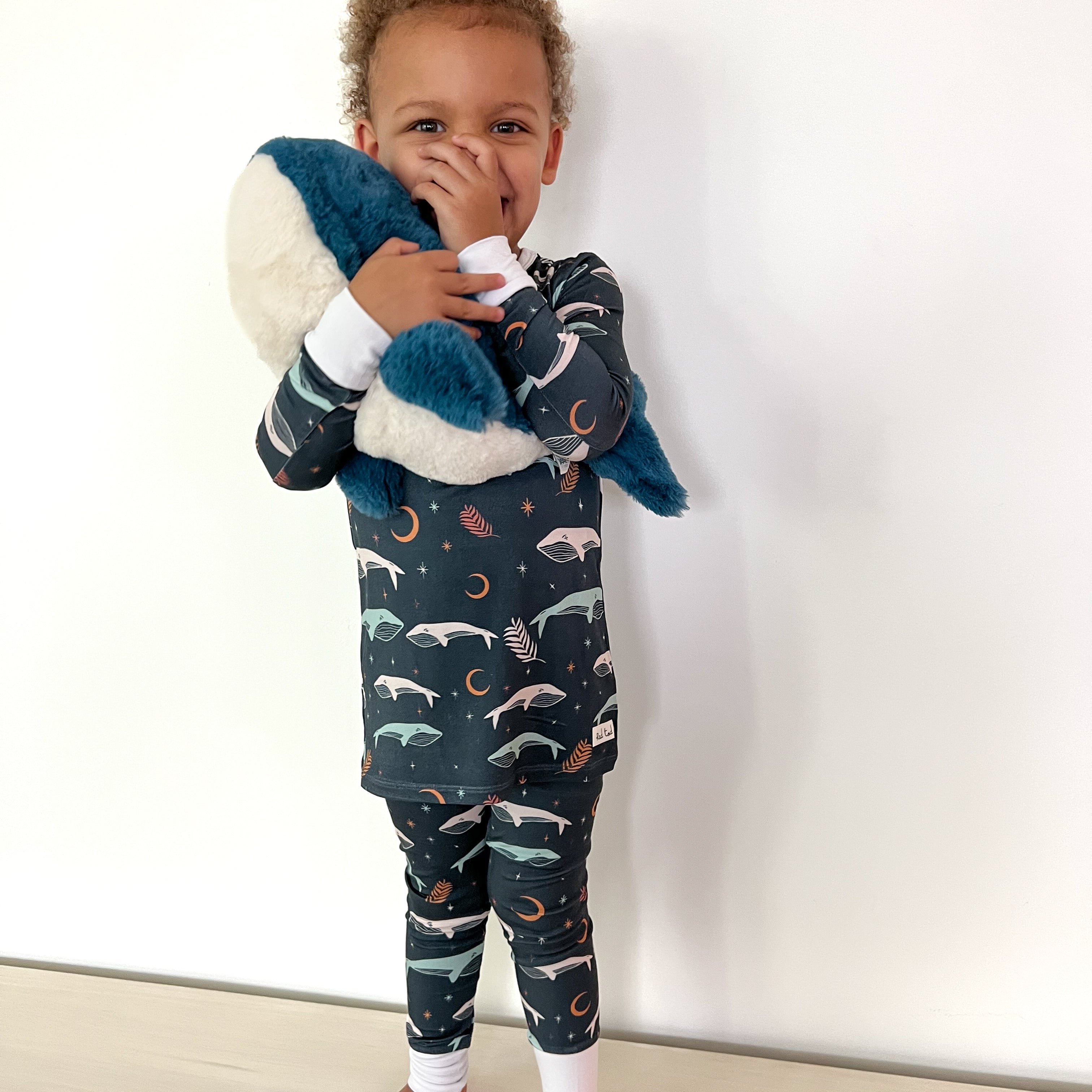 boy holding plush whale while wearing Luna Whale Bamboo Onesie featuring soft, breathable fabric, hypoallergenic properties, and a cute whale design for ultimate comfort and style