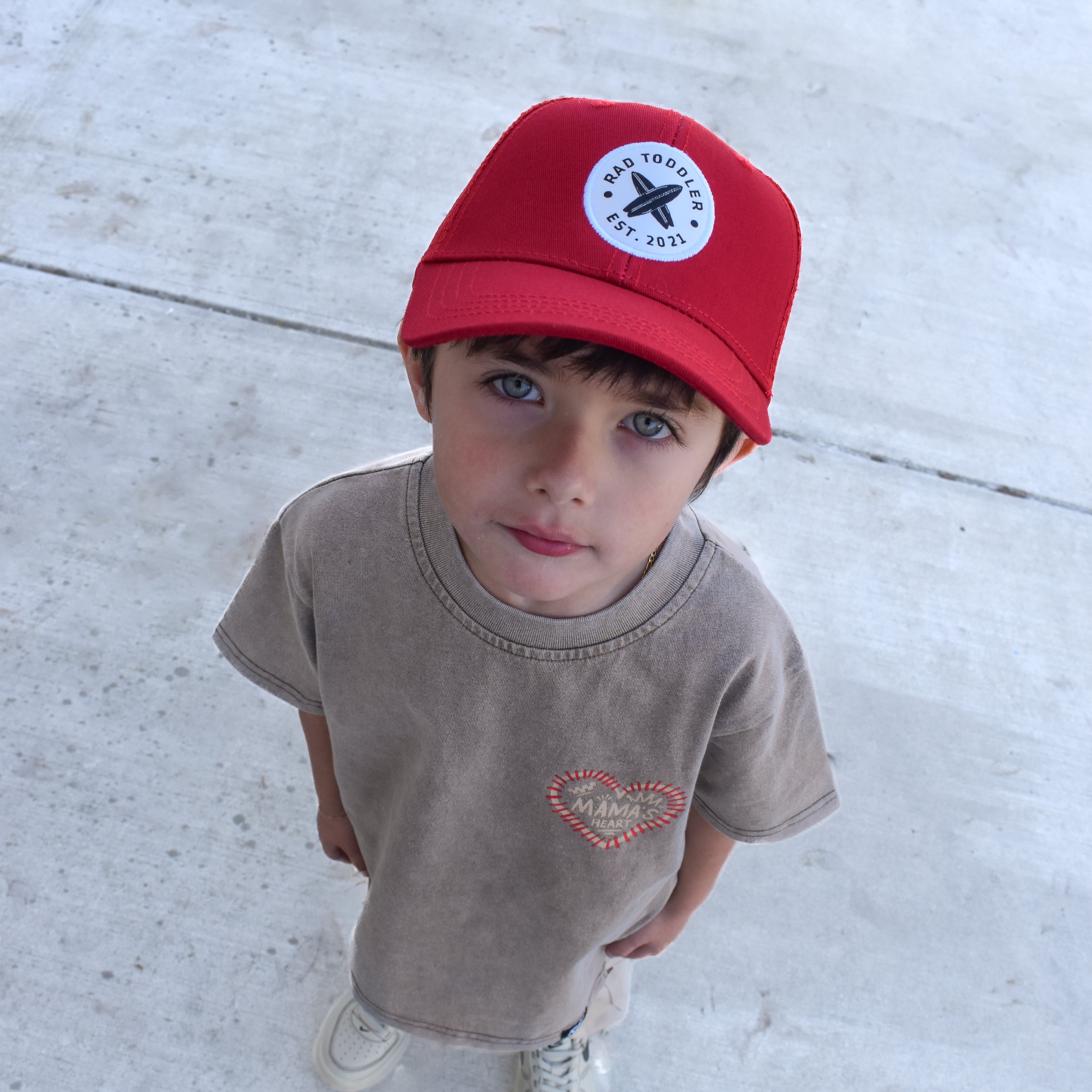 Child wearing a red cap and beige t-shirt on a concrete surface