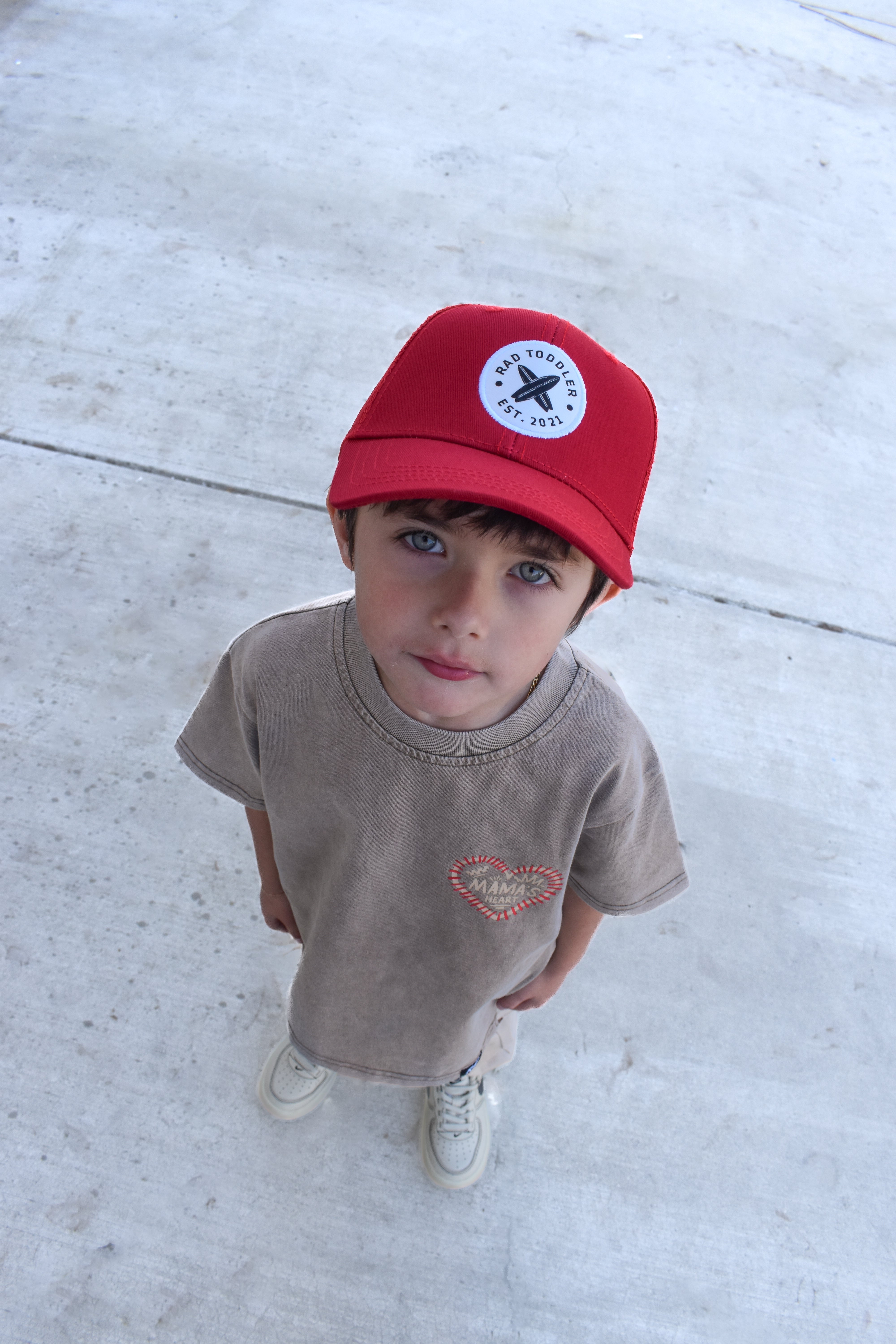 Child wearing a red cap and beige t-shirt on a concrete surface