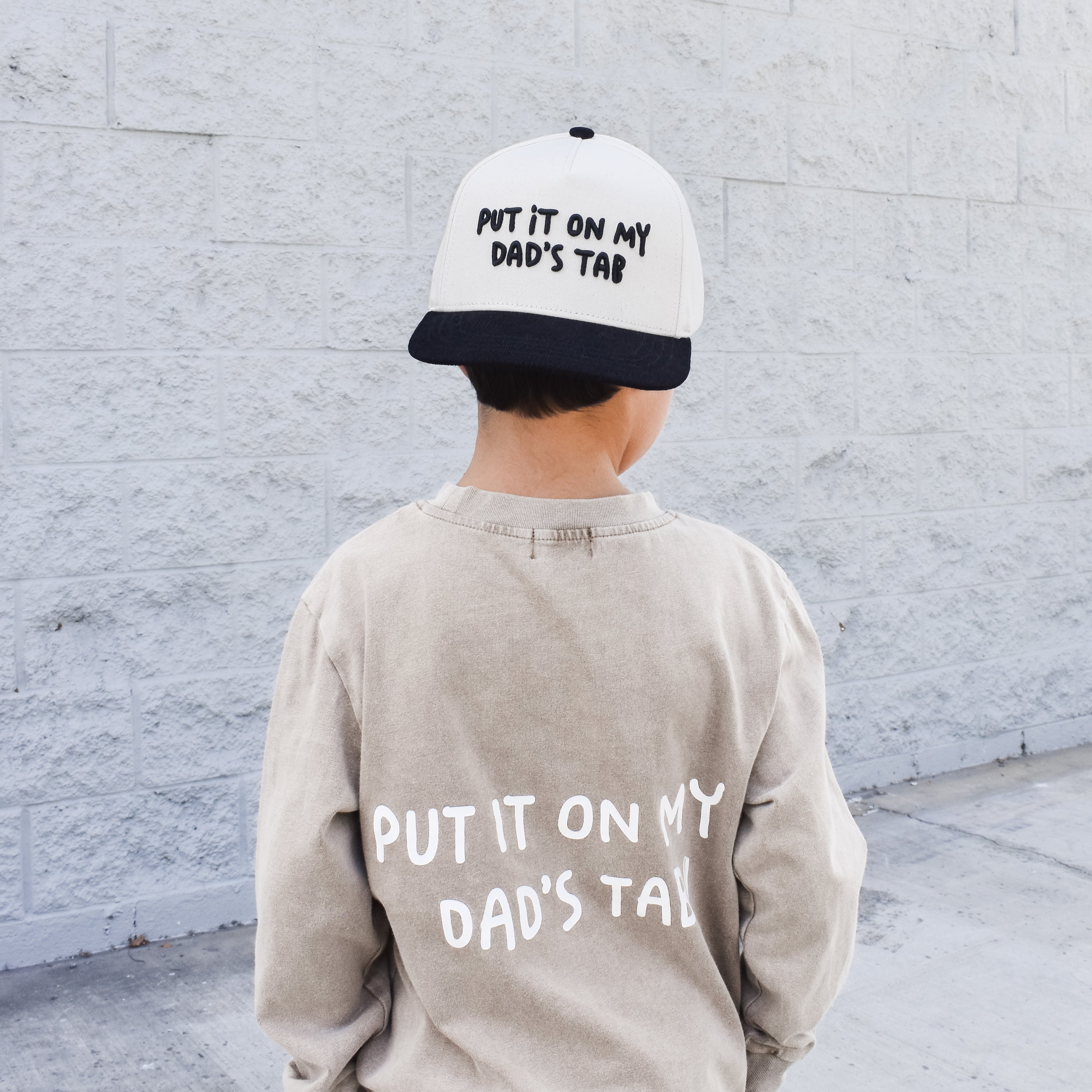 Child wearing Put It On My Dad’s Tab snapback outdoors while playing and also wearing the matching shirt