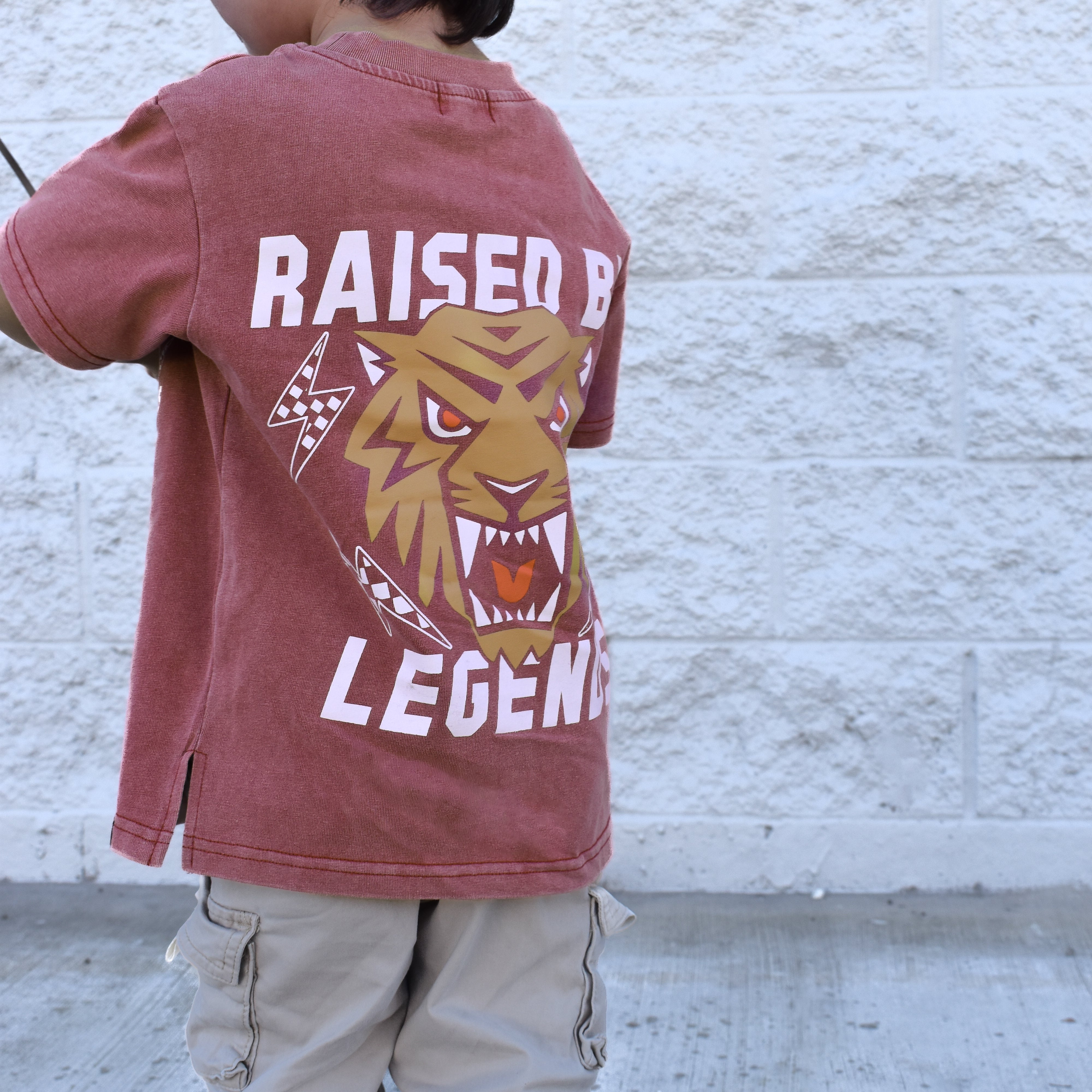 Kid wearing Raised by Legends tiger tee, red acid wash premium kids shirt